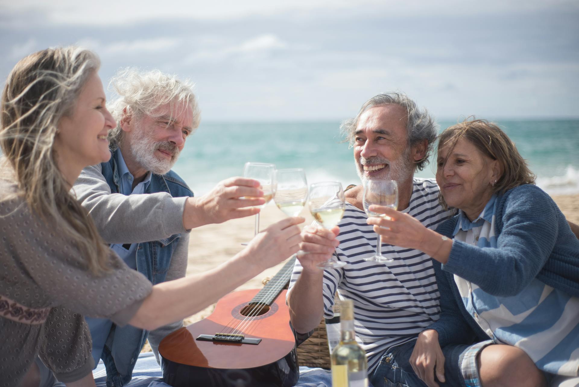 Grauhaarige Menschen stoßen mit Weingläsern am Strand an | Quelle: Pexels