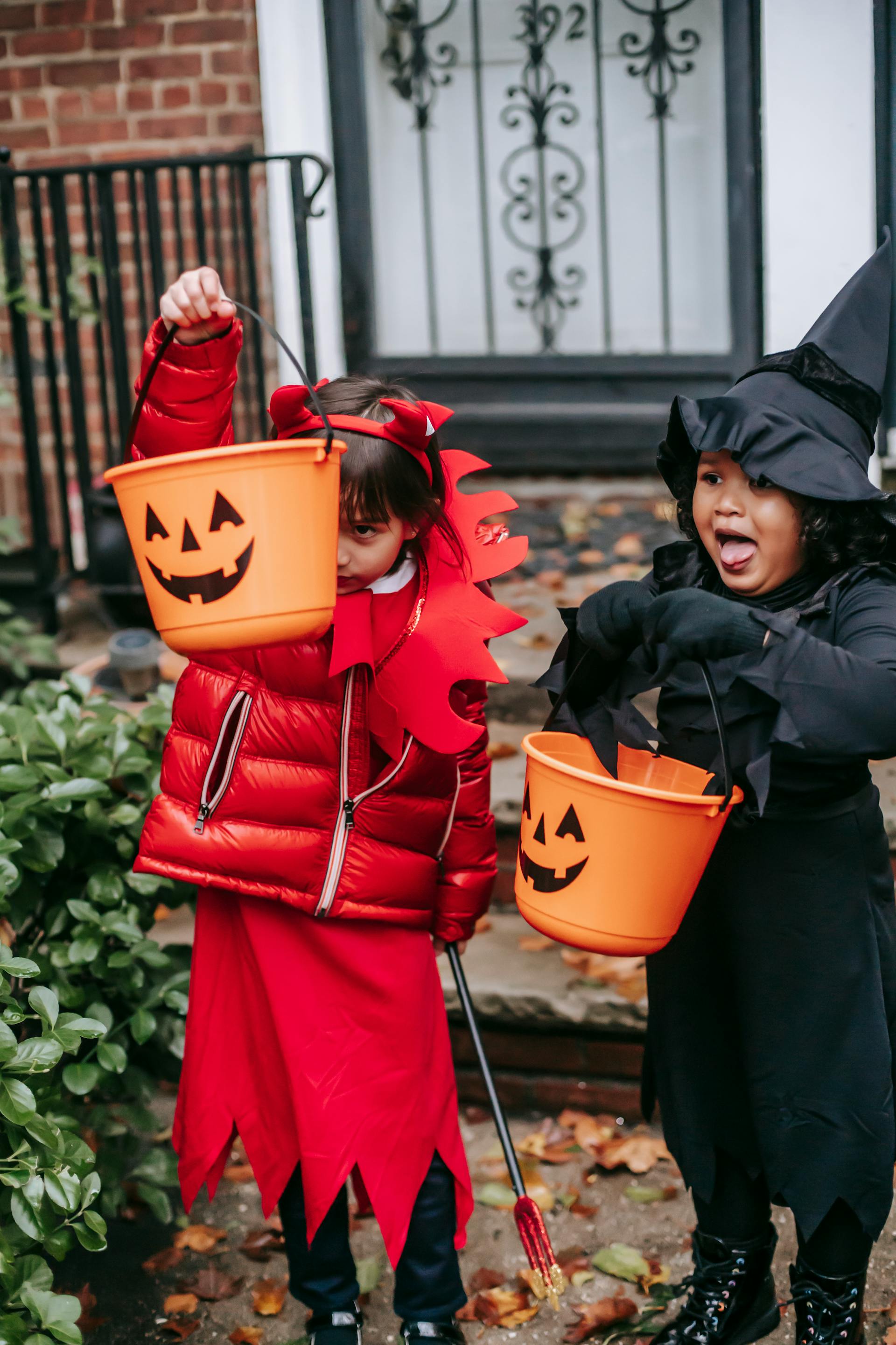 Kinder, die in Halloween-Kostümen vor einem Hauseingang Süßes oder Saures spielen | Quelle: Pexels