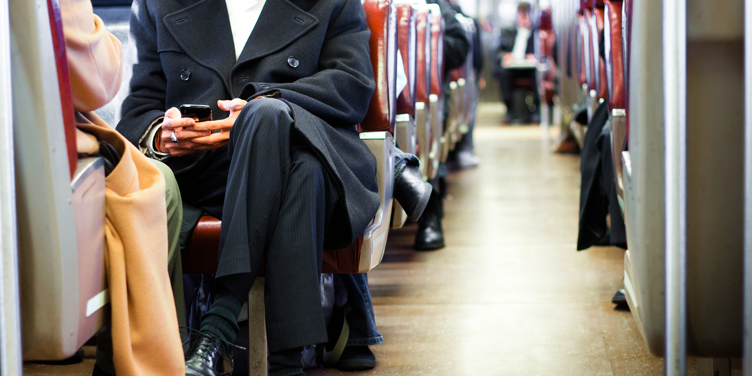 Ein Mann im Anzug sitzt in einem belebten Zug | Quelle: Shutterstock