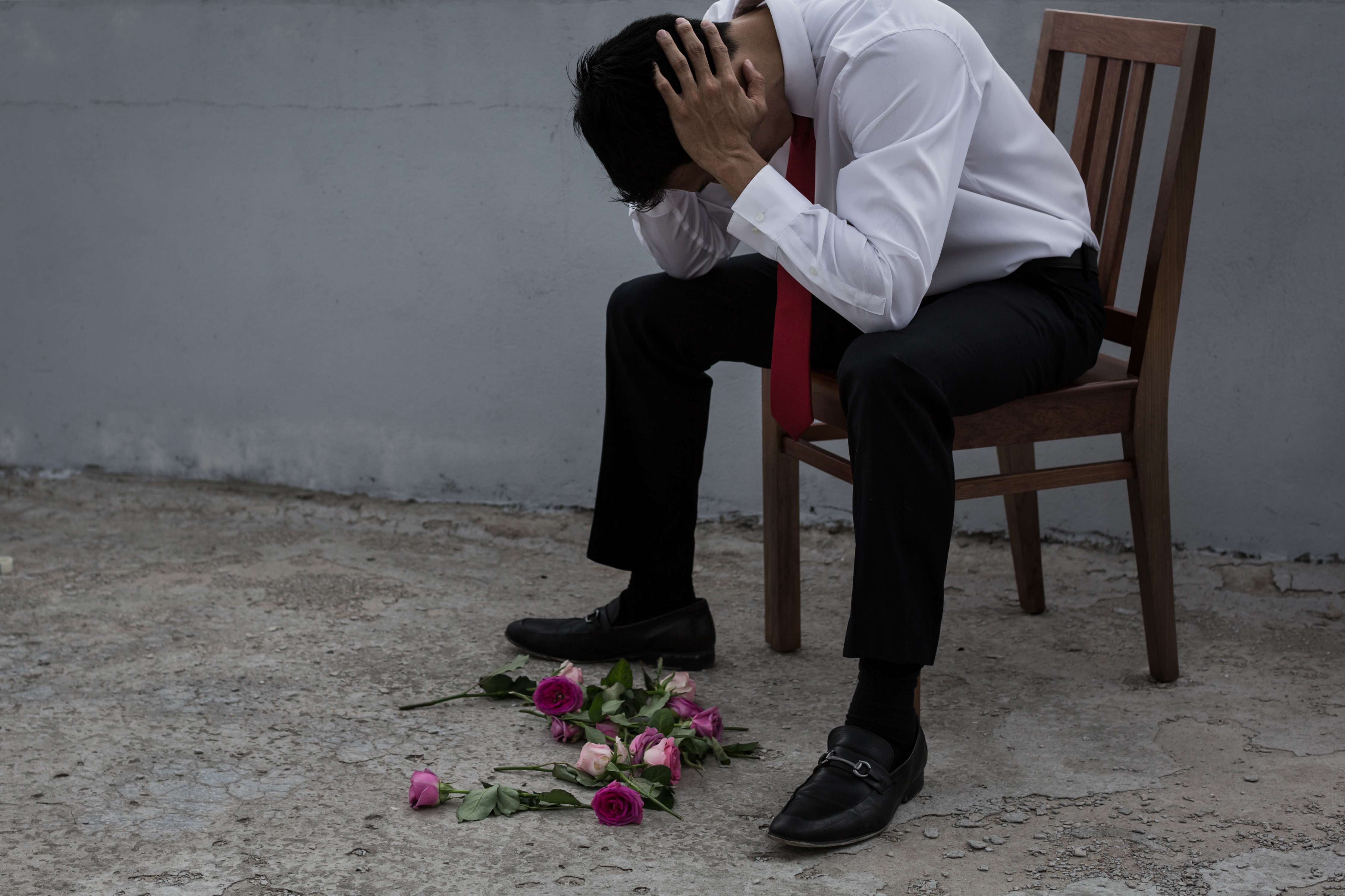 Ein traurig dreinblickender Mann mit auf dem Boden verstreuten Blumen | Quelle: Shutterstock