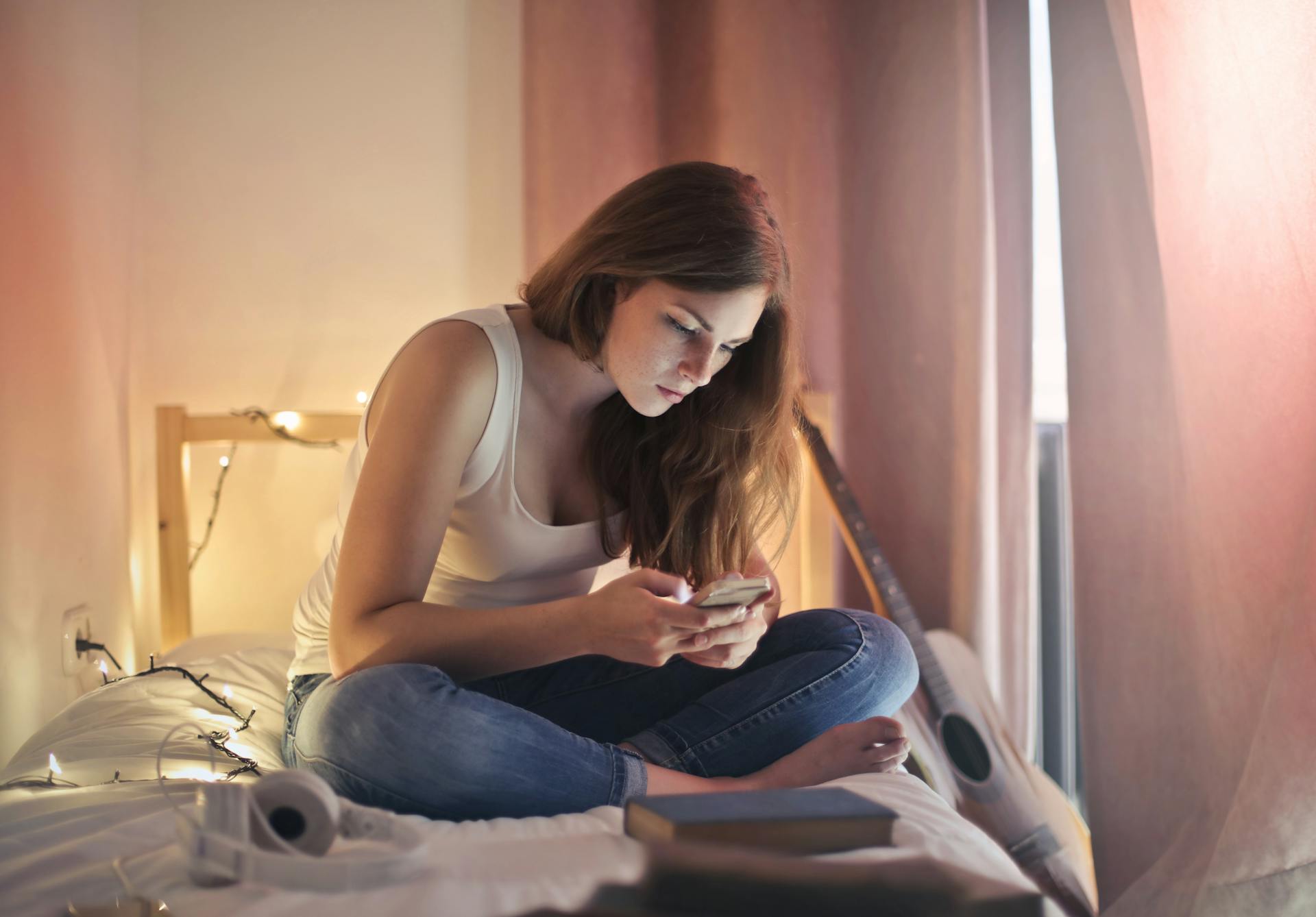 Eine Frau, die ihr Telefon benutzt, während sie auf ihrem Bett sitzt | Quelle: Pexels