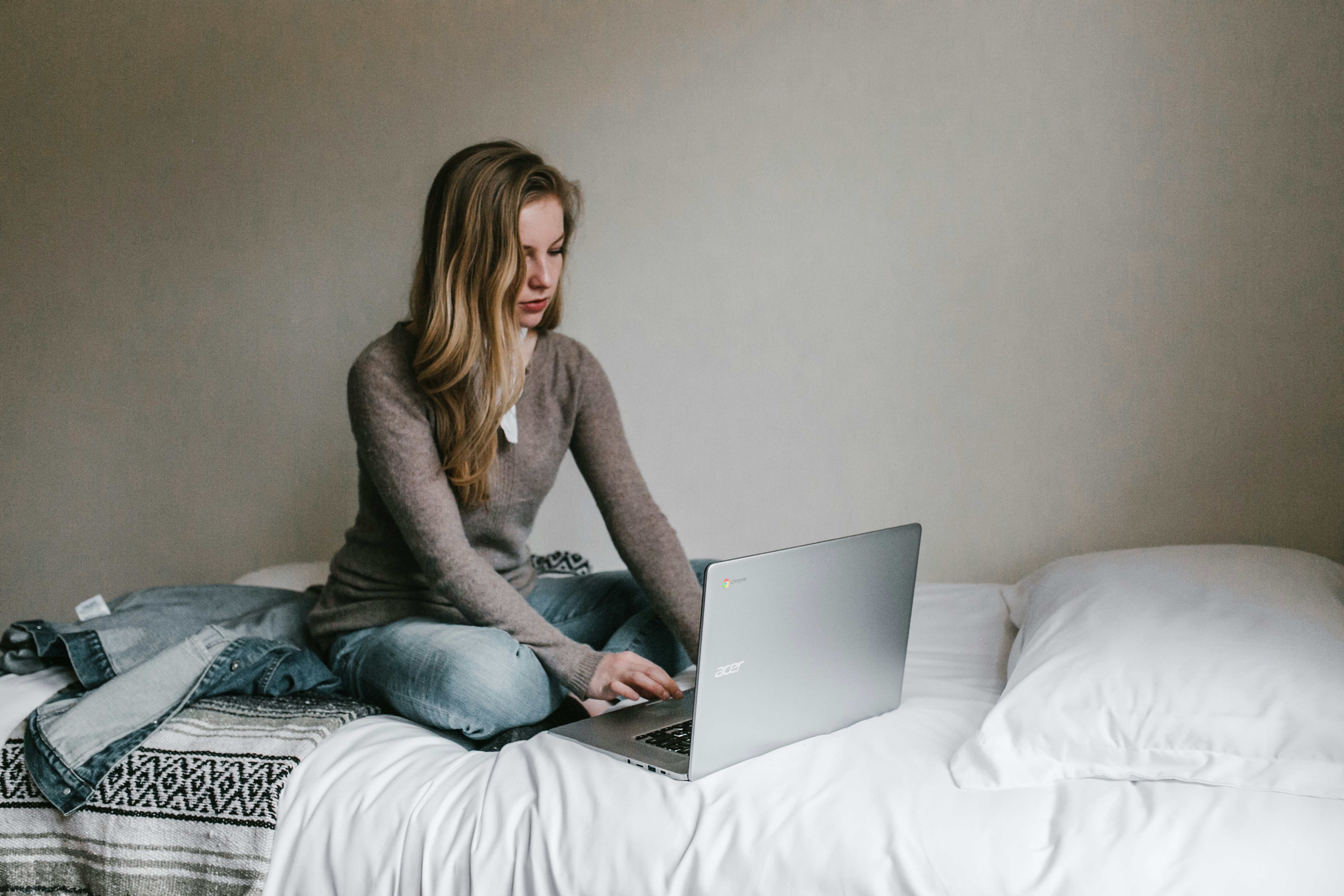 Eine Frau, die auf einem Bett sitzend an einem Laptop arbeitet | Quelle: Unsplash