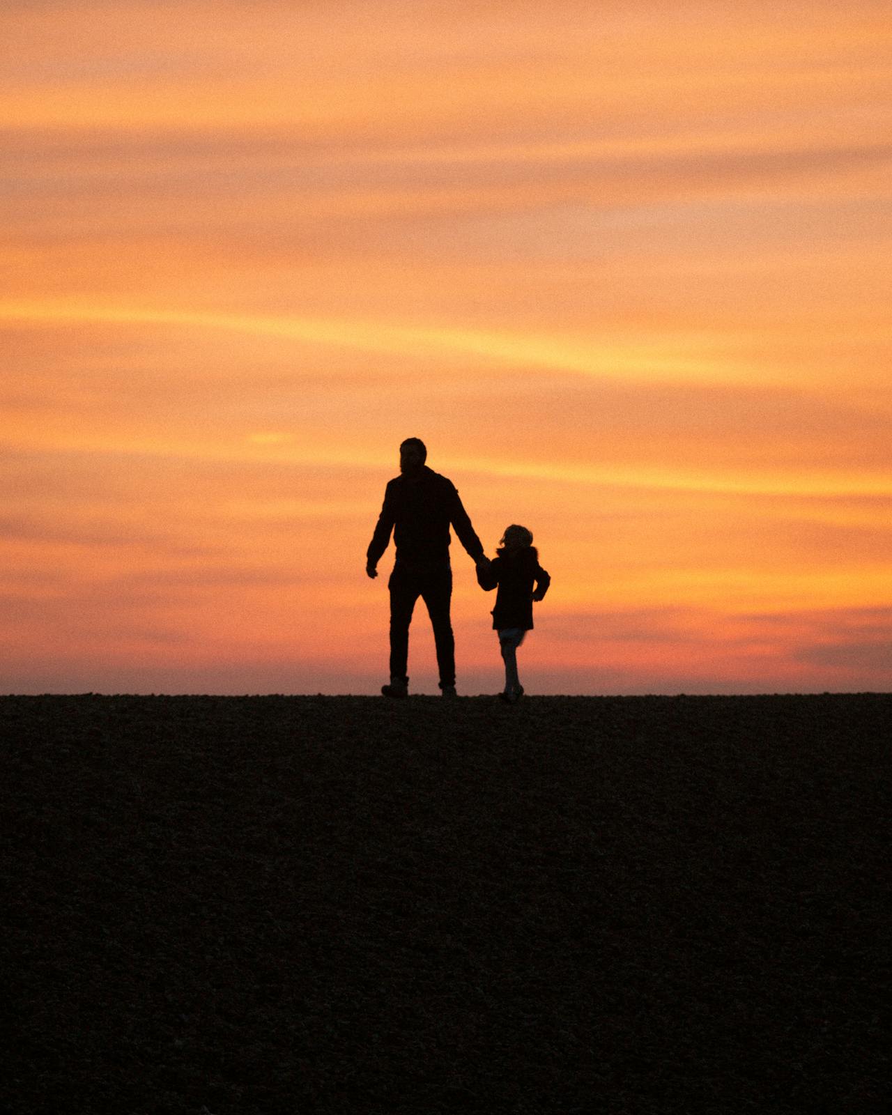 Silhouette eines Mannes, der mit seiner kleinen Tochter spazieren geht | Quelle: Pexels