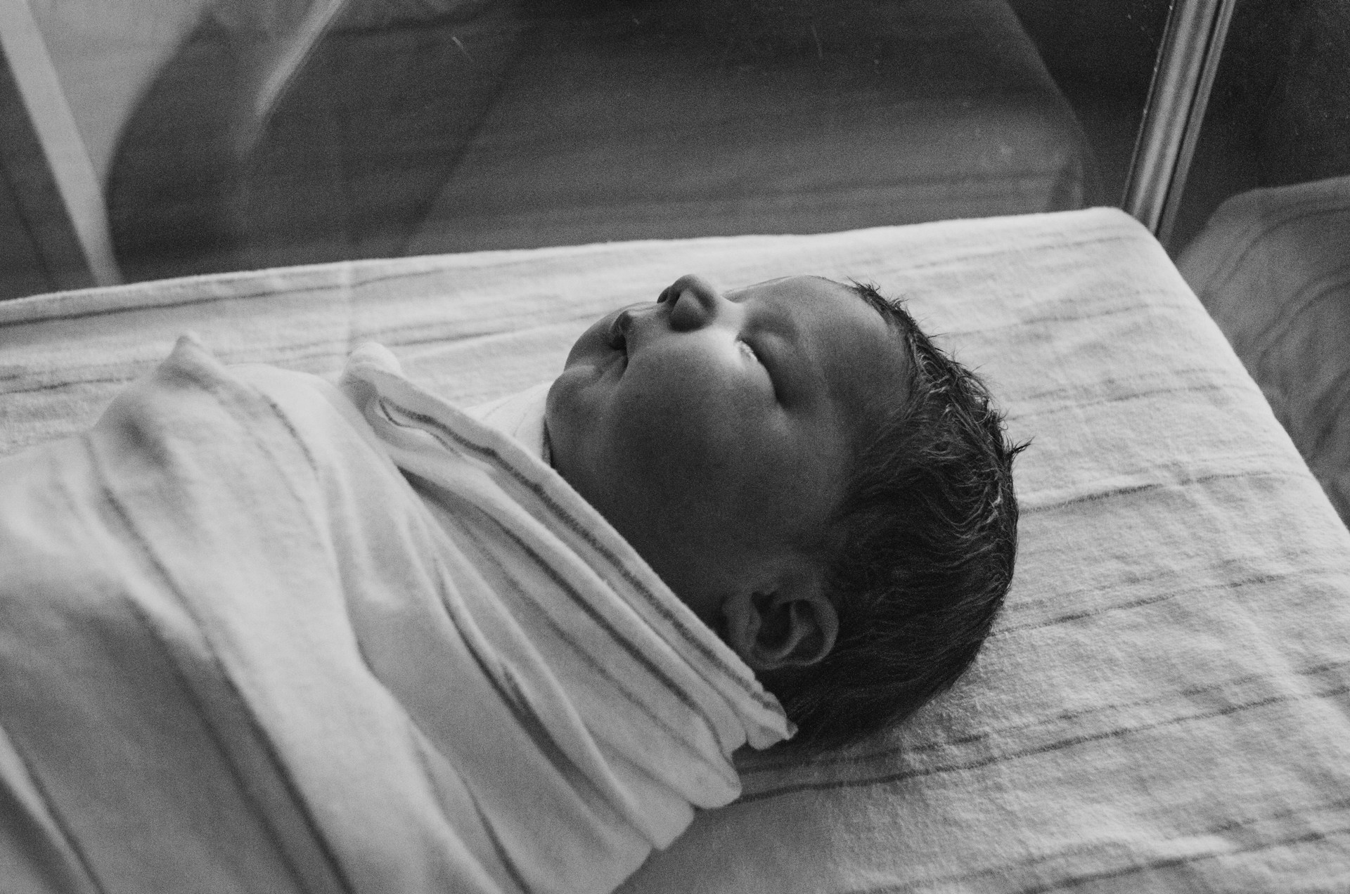 Graustufenaufnahme eines neugeborenen Babys in einem Stubenwagen | Quelle: Unsplash