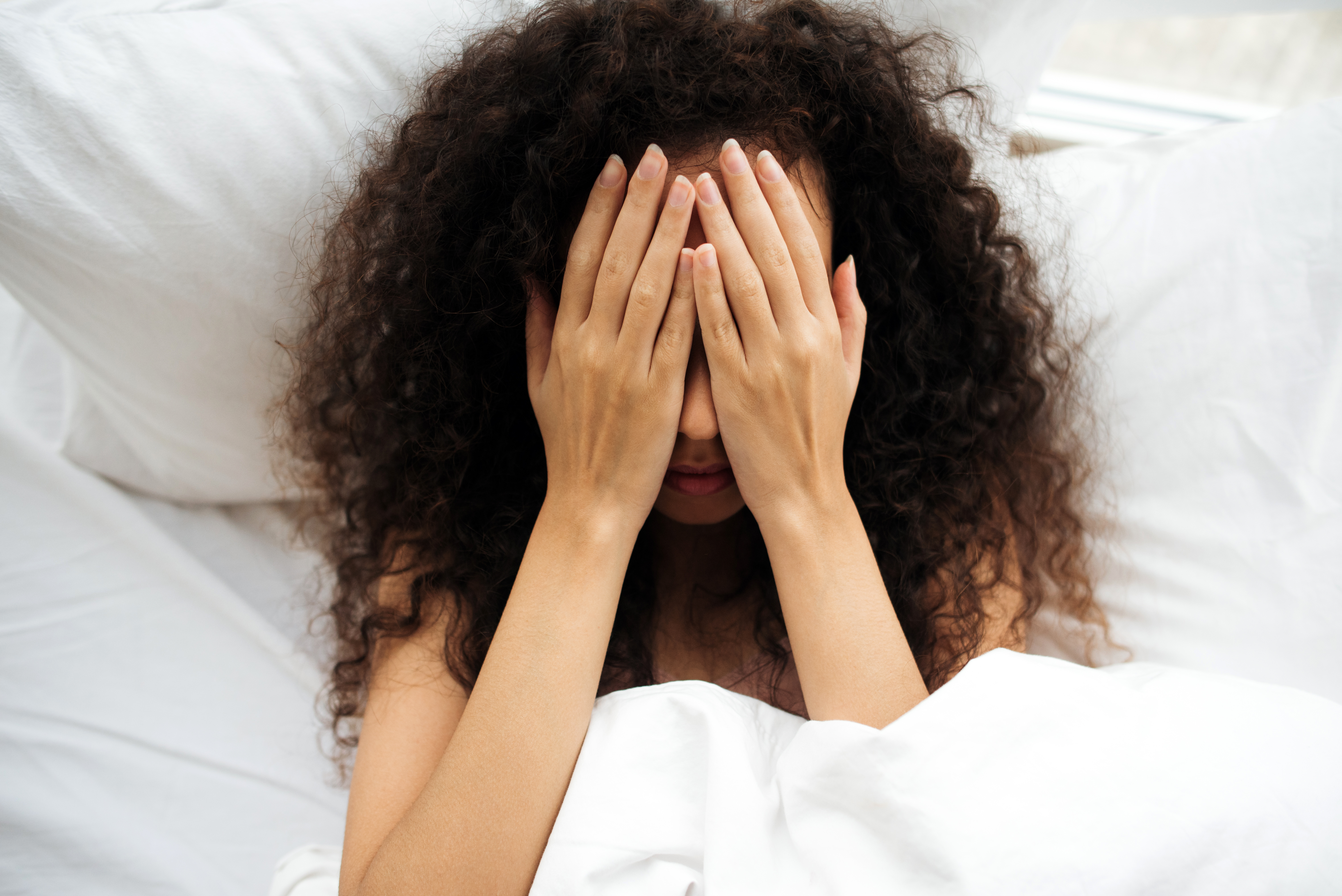 Frau im Bett, die ihr Gesicht mit den Händen bedeckt | Quelle: Getty Images