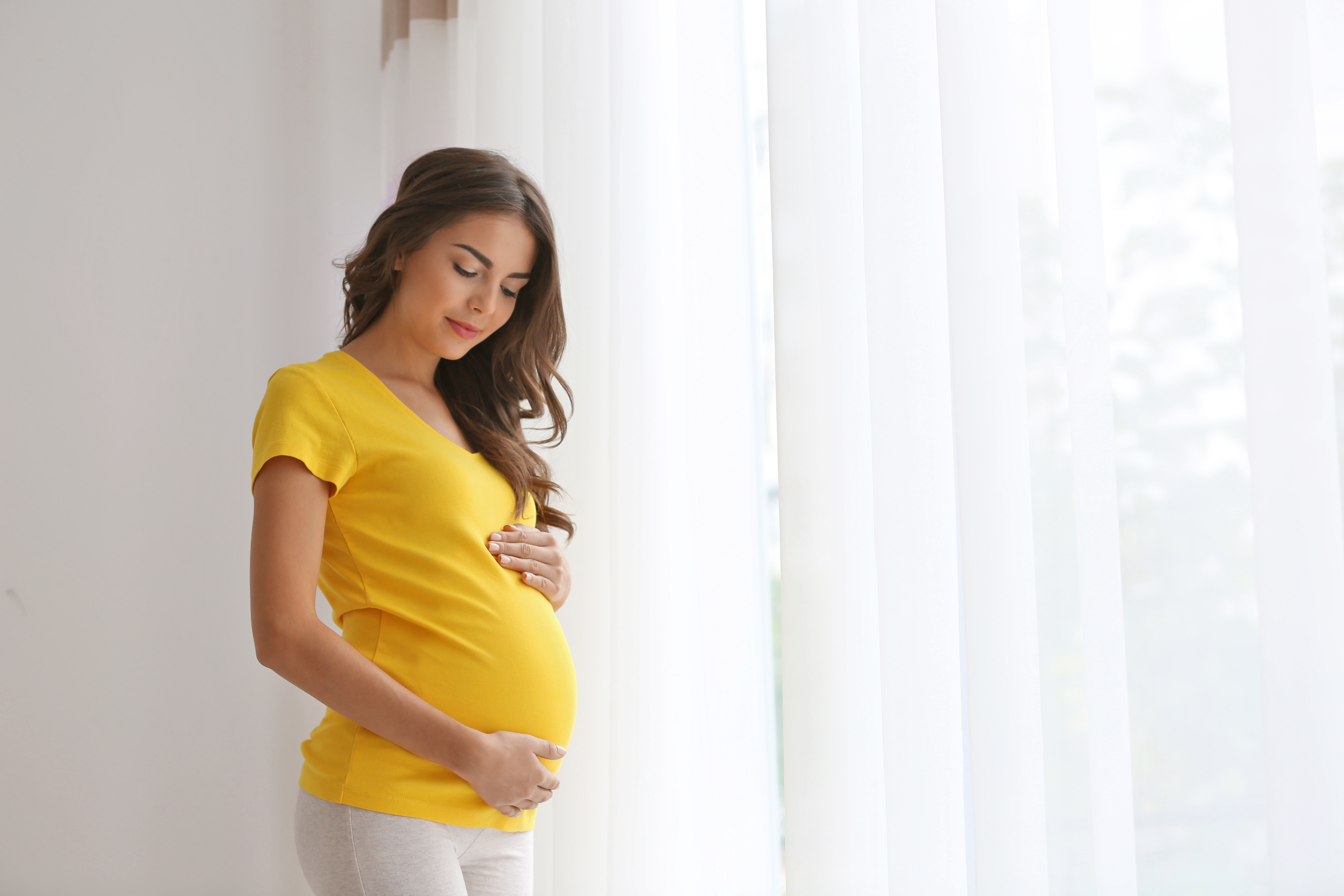 Eine schwangere Frau in einem gelben Shirt, die ihren Bauch hält | Quelle: Shutterstock