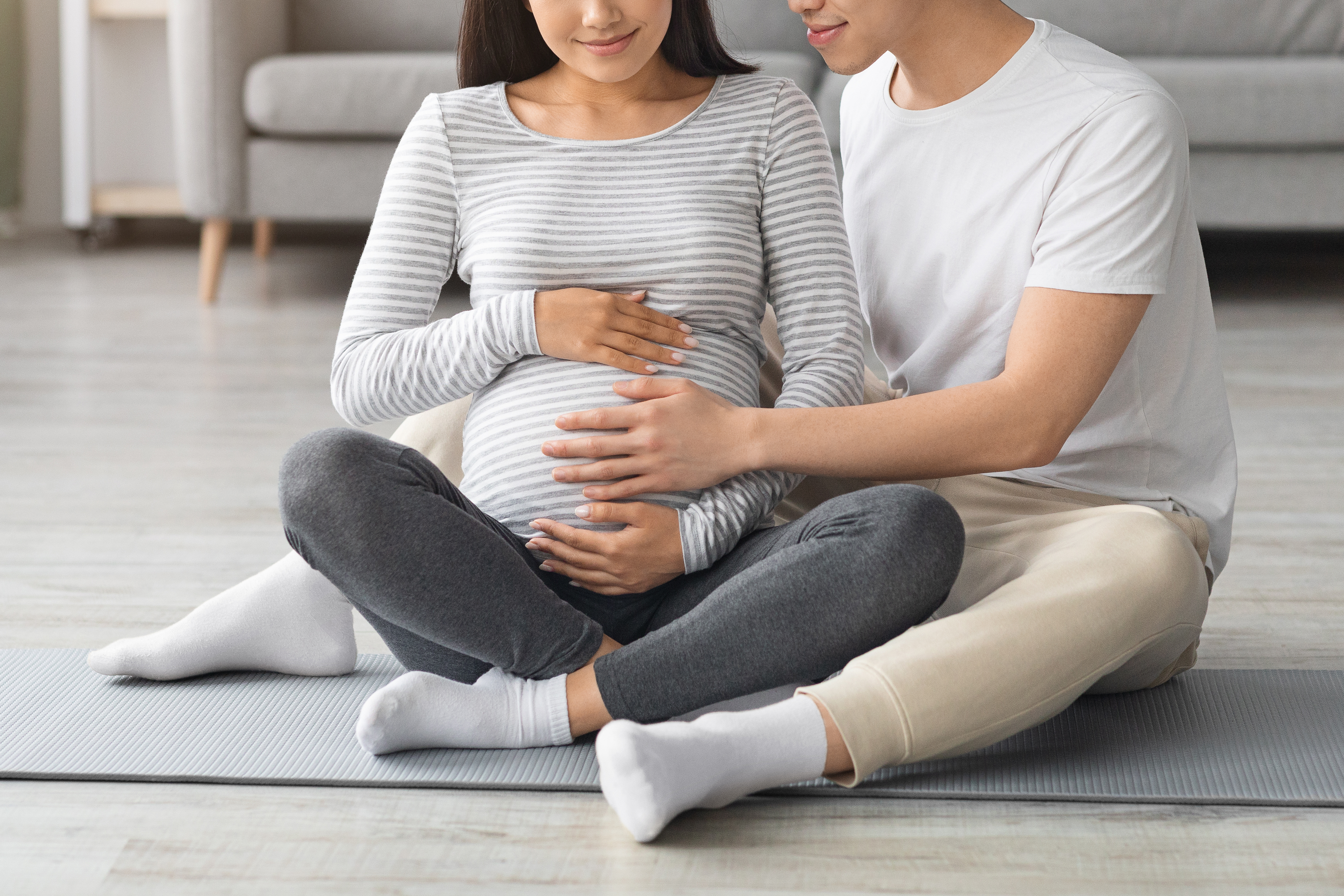 Ein Mann sitzt mit seiner schwangeren Frau auf einer Yogamatte | Quelle: Shutterstock