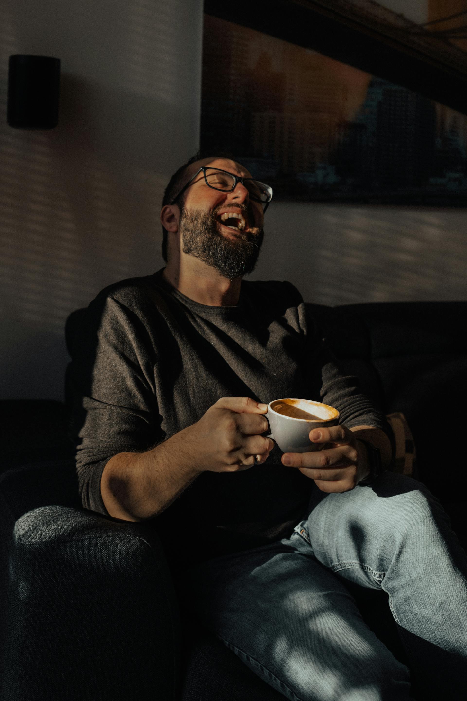 Ein Mann lacht, während er eine Tasse Kaffee in der Hand hält | Quelle: Pexels