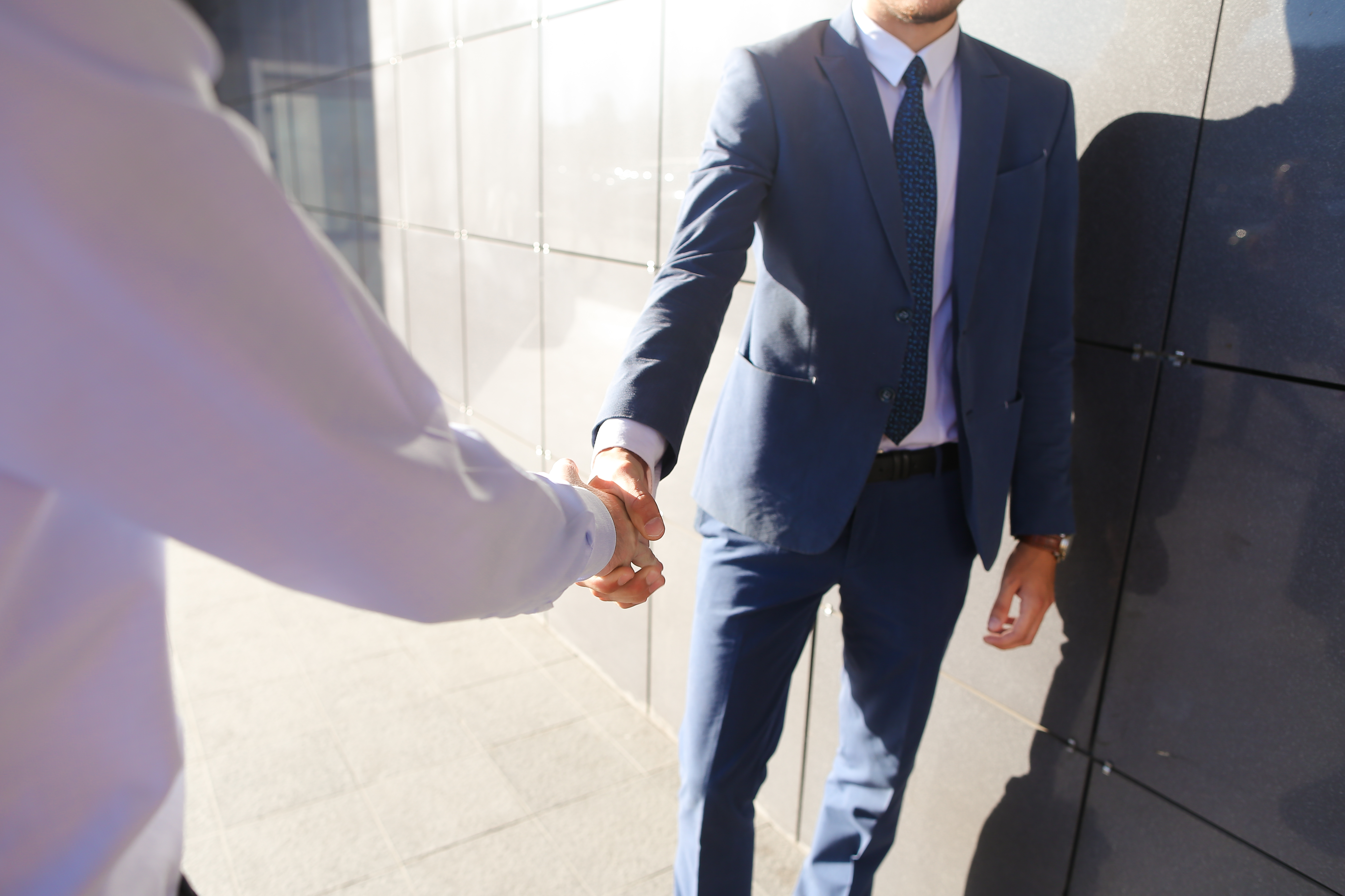 Freunde treffen sich und begrüßen sich mit Handschlag an der grauen Wand des Business Centers im Freien. | Quelle: Shutterstock