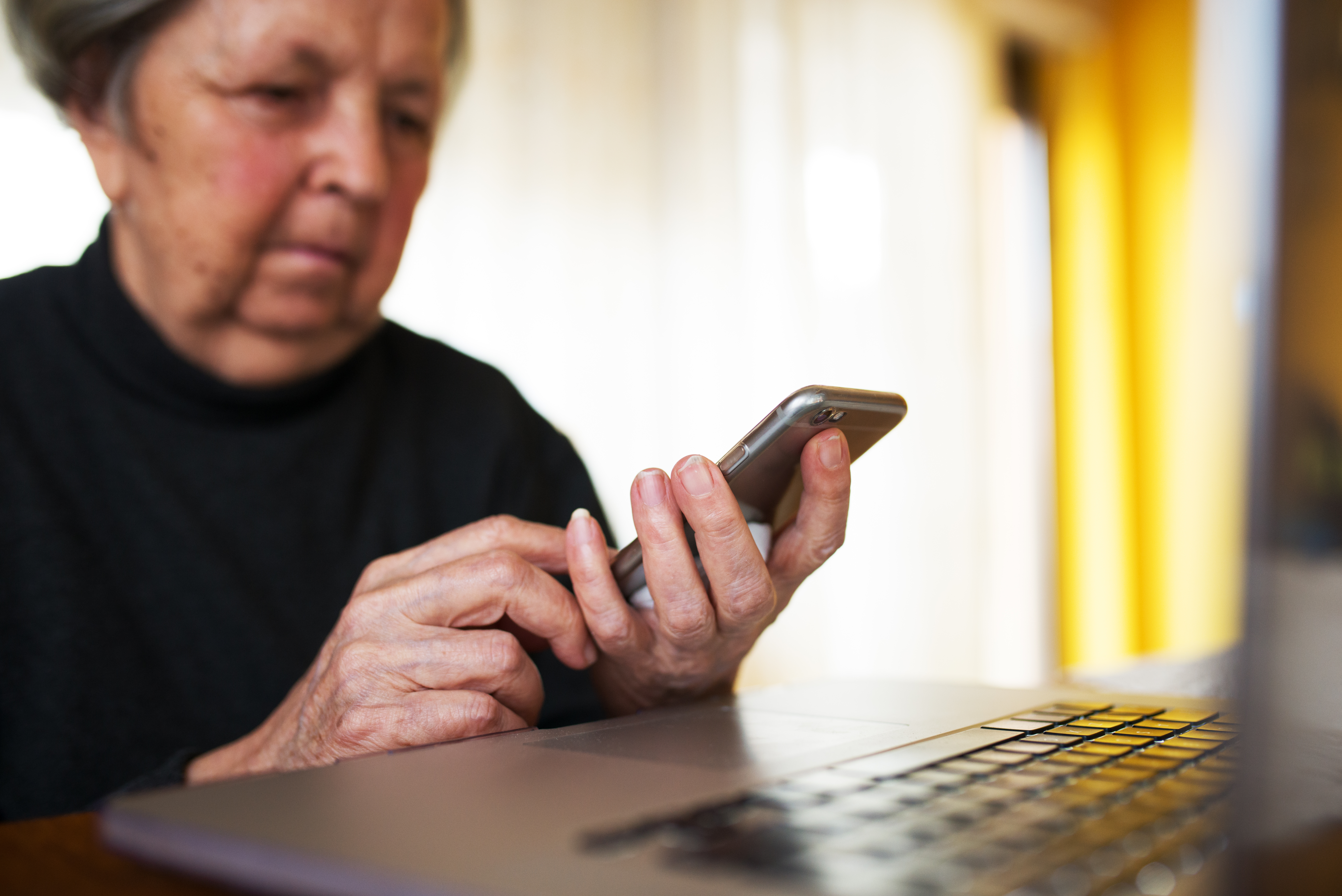 Eine ältere Frau, die zu Hause ein Smartphone und einen Laptop benutzt | Quelle: Shutterstock