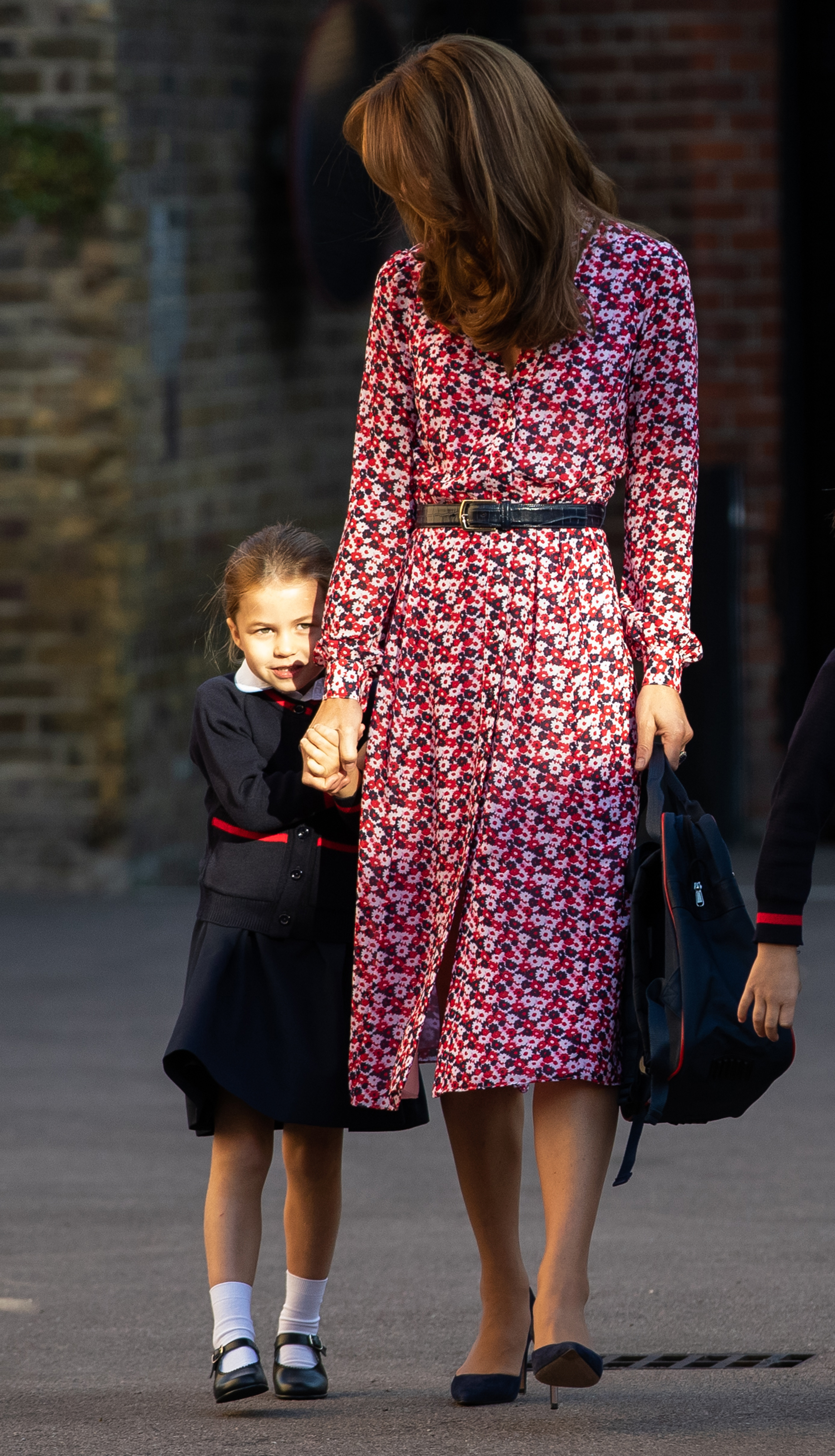 Prinzessin Charlotte hält die Hand ihrer Mutter Catherine, als sie am 5. September 2019 in London, England, zu ihrem allerersten Schultag an der Thomas’s Battersea ankommt. Die junge Royal blickt schüchtern zu den Schaulustigen hinüber – in ihrem marineblau-roten Schuluniformrock, einer Strickjacke, weißen Söckchen und schwarzen Mary-Jane-Schuhen –, begleitet von der Herzogin in einem rosa-marineblauen Midikleid mit Blumenmuster und Gürtel sowie spitzen marineblauen Pumps. | Quelle: Getty Images