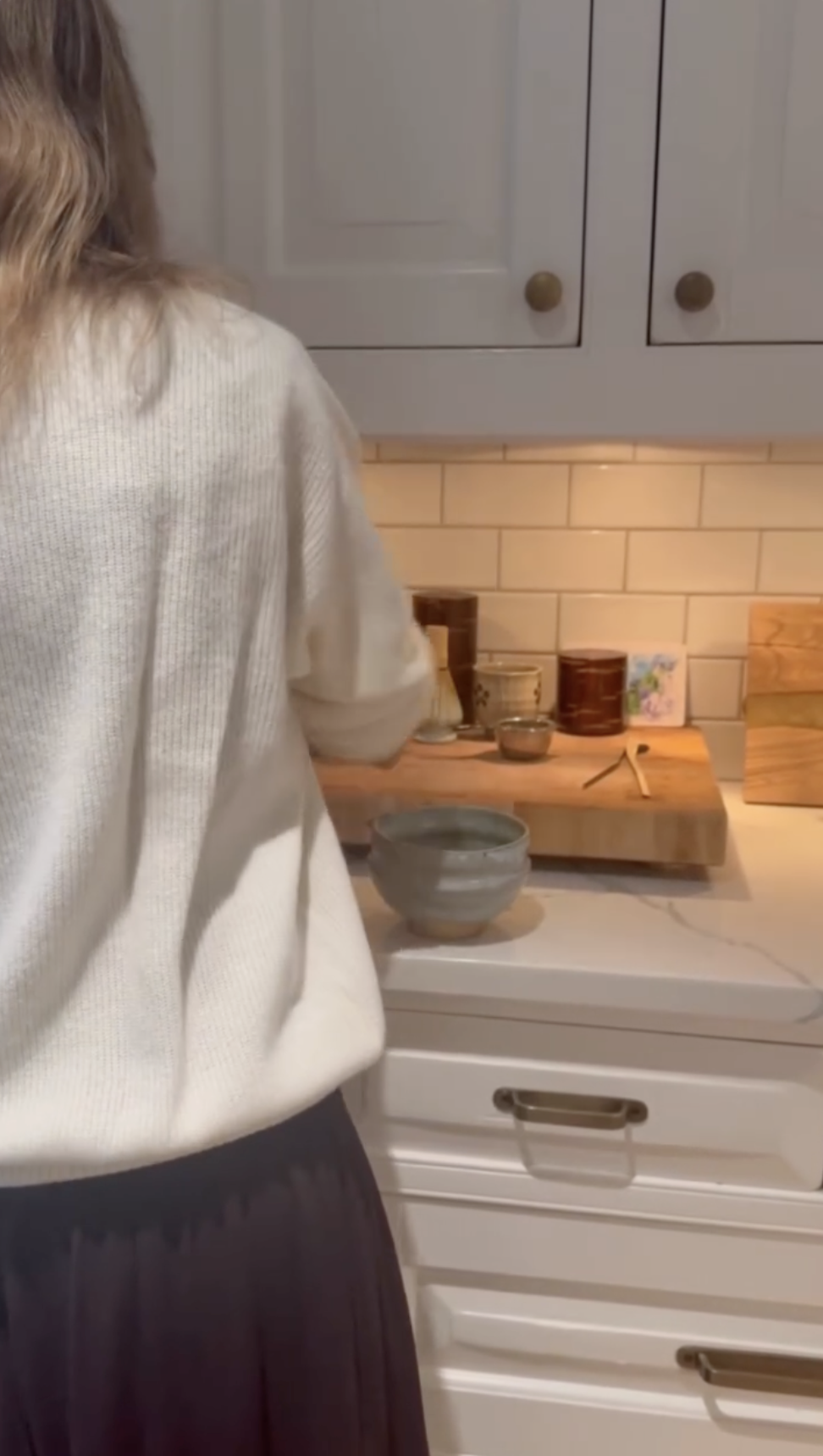 Alejandra Silva steht an der Küchentheke im Haus der Familie in Spanien und gewährt einen Blick auf den hellen Raum mit weißen Schränken, Fliesenspiegeln im Subway-Stil und warmer Unterbauleuchte. | Quelle: Instagram/alejandragere