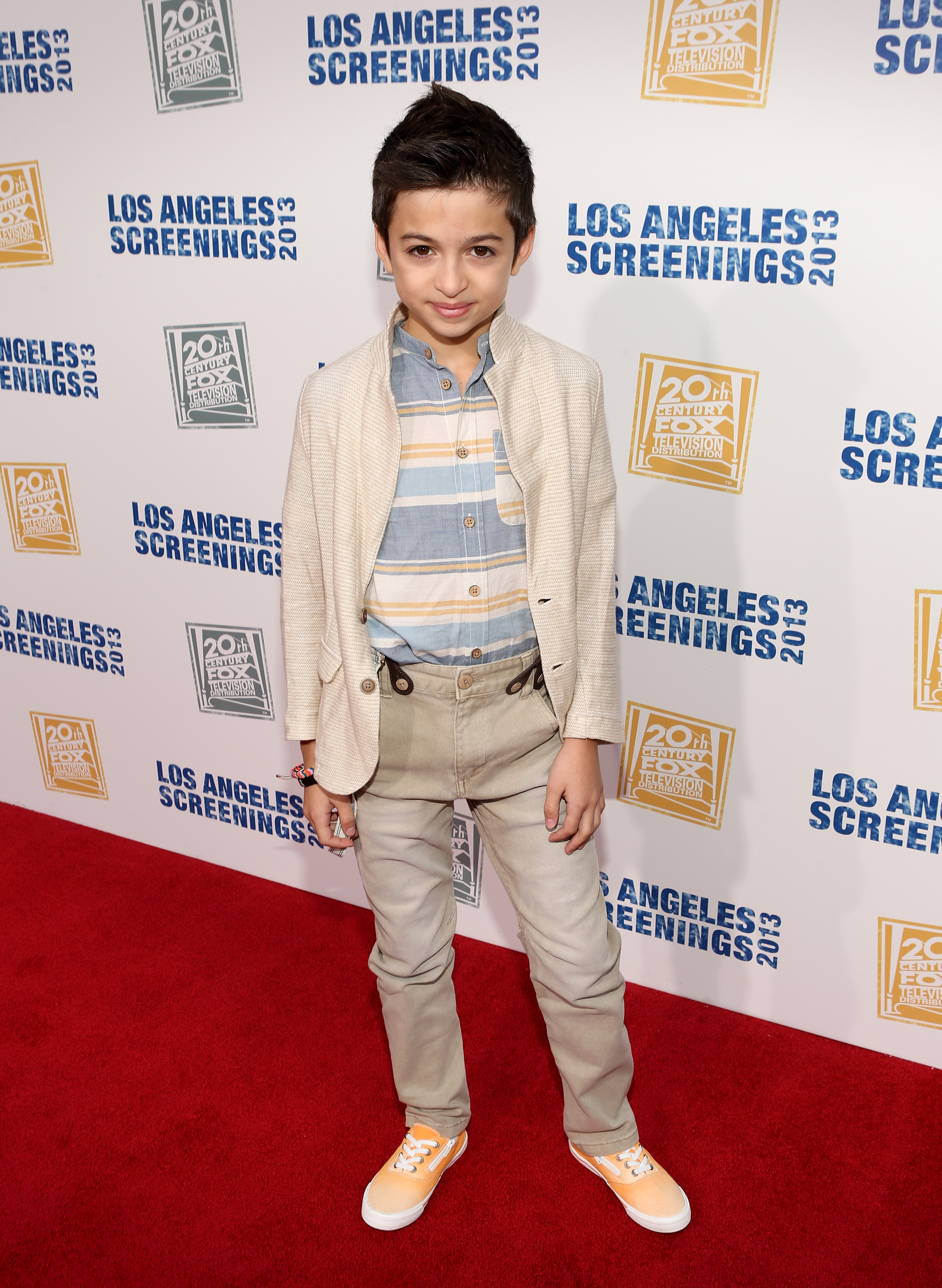 Sie posiert auf dem roten Teppich bei der „LA Screenings Lot Party 2013“ von Twentieth Century Fox Television Distribution in Los Angeles, Kalifornien, und trägt einen cremefarbenen Blazer, ein gestreiftes Hemd, eine beige Hose und orangefarbene Sneaker. | Quelle: Getty Images