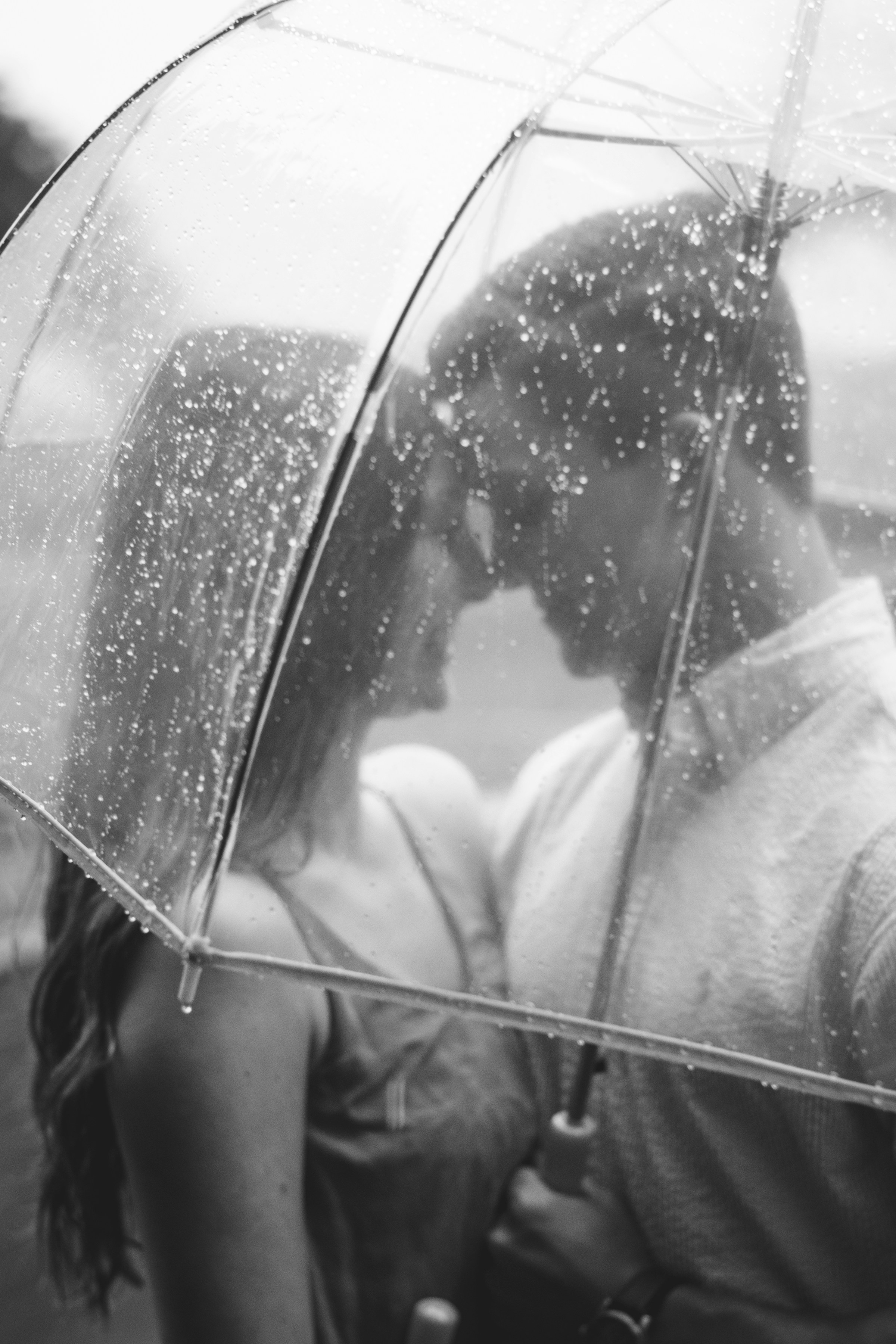 Ein junges romantisches Paar unter einem durchsichtigen Regenschirm an einem regnerischen Tag | Quelle: Unsplash