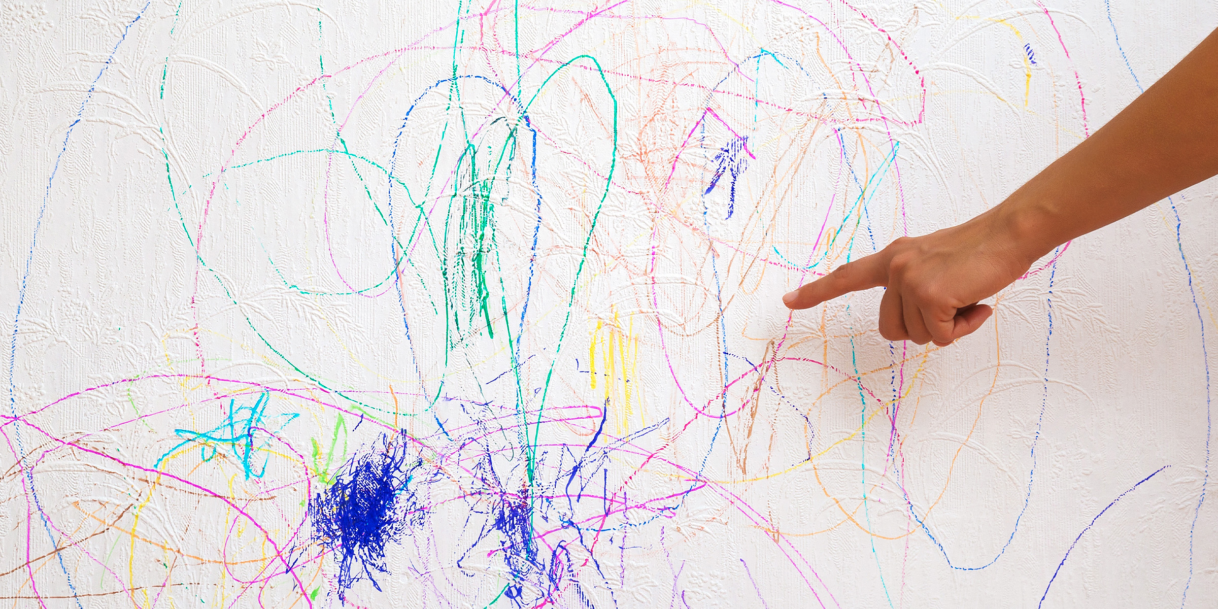 Ein Finger, der auf buntes Gekritzel an einer Wand zeigt | Quelle: Shutterstock
