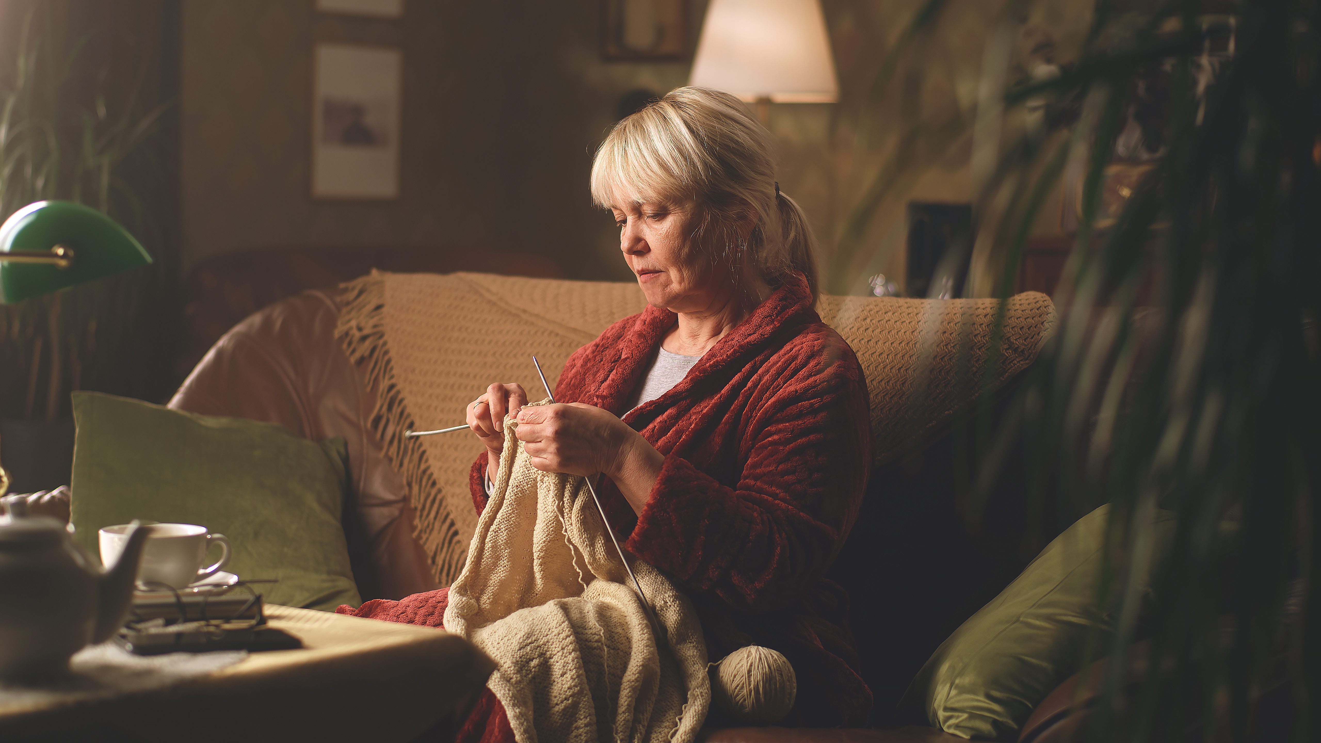 Eine ältere Frau strickt einen Pullover, während sie auf dem Sofa sitzt | Quelle: Shutterstock