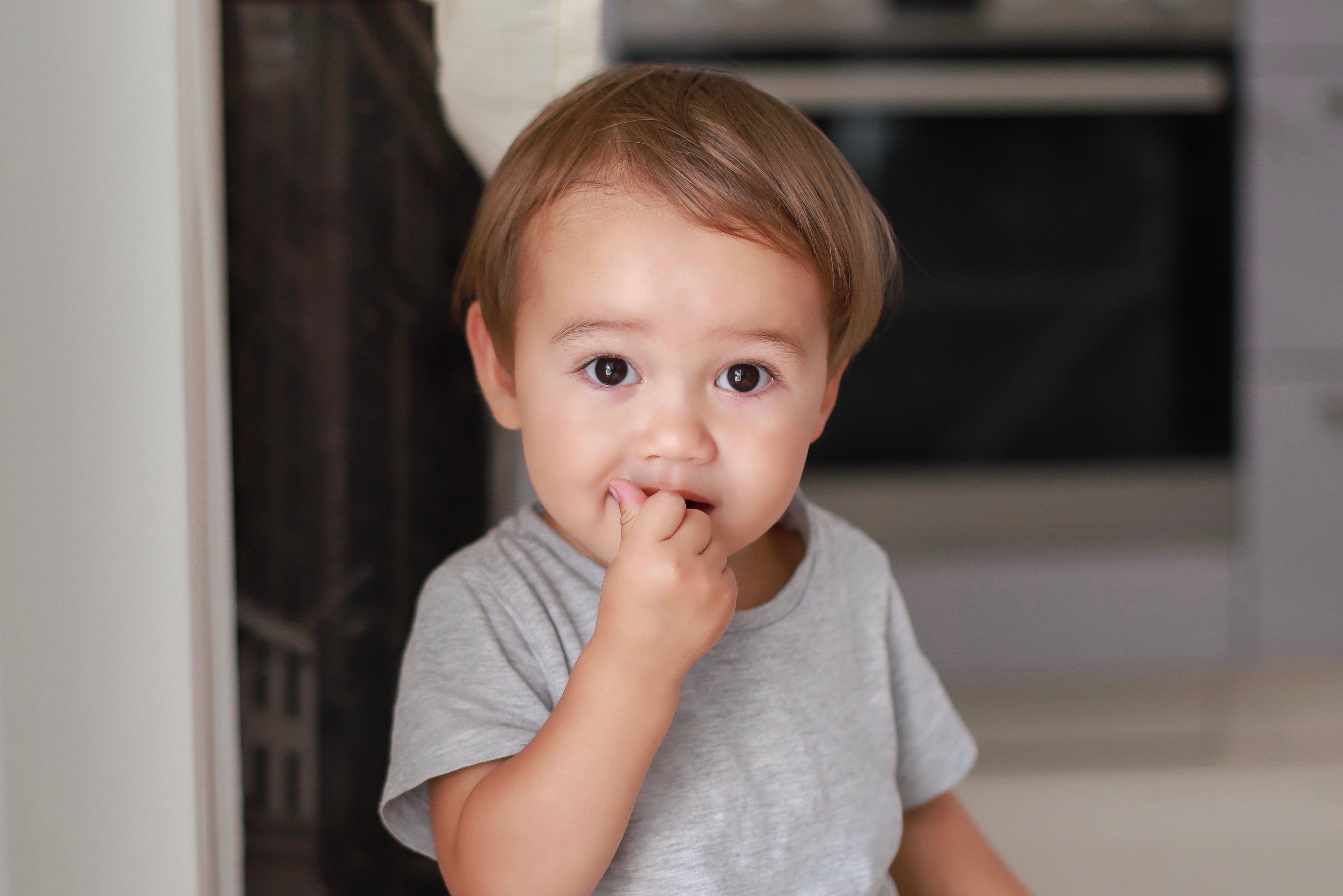 Kopfbild eines kleinen Jungen mit Finger im Mund, der zu Hause einen Snack isst. | Quelle: Shutterstock
