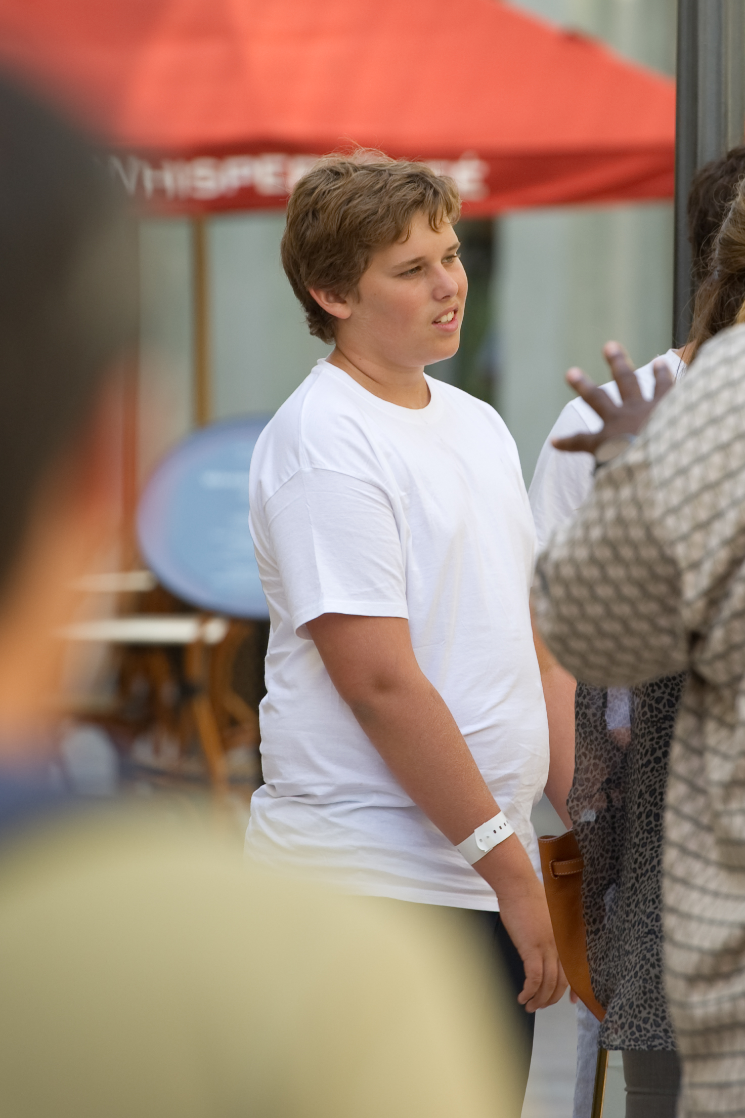 Dieses Foto wurde ebenfalls am selben Tag im The Grove aufgenommen und zeigt Christopher, der während eines Gesprächs aufmerksam zuhört. Sein jugendliches Gesicht und sein kurzes, zerzaustes Haar umrahmen seinen Ausdruck, während an seinem linken Handgelenk ein weißes Armband zu sehen ist.