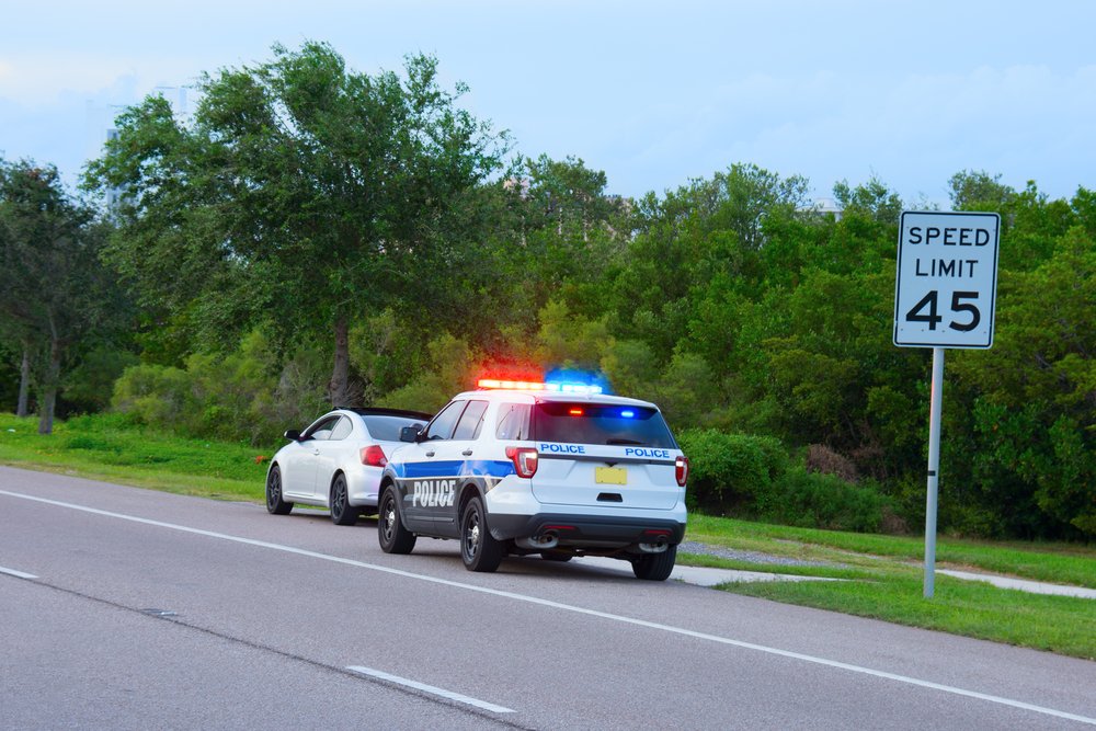 Ein Polizeifahrzeug mit blinkendem Rot- und Blaulicht hat hinter einem Auto angehalten. | Quelle: Shutterstock 