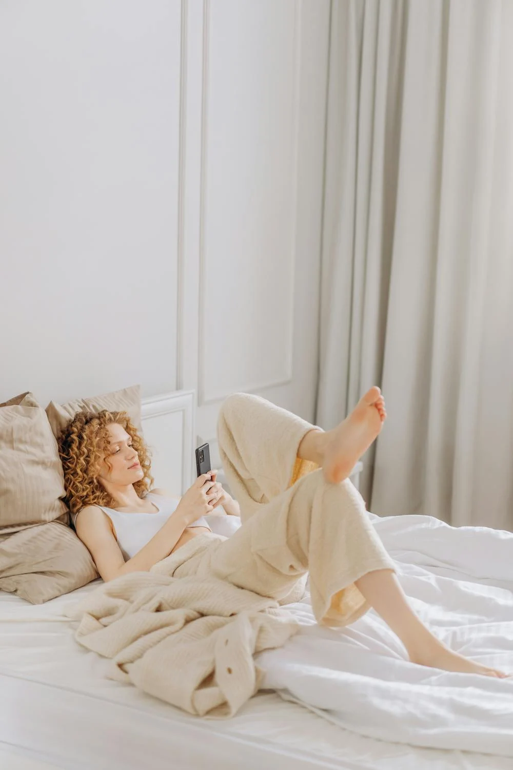 Uma mulher feliz ao telefone na cama ⏐ Fonte: Pexels