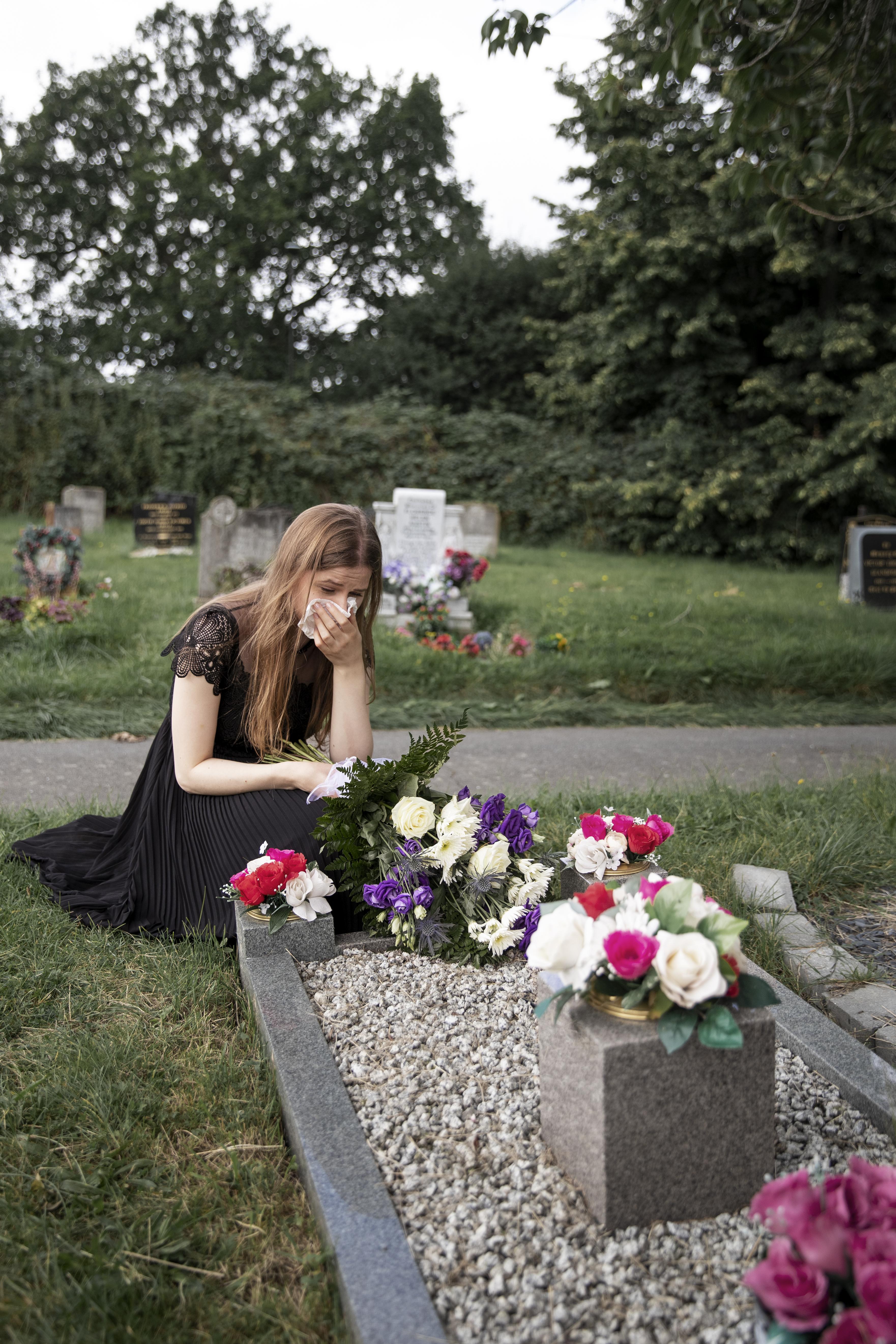 Eine trauernde junge Frau vor einem Grab auf einem Friedhof | Quelle: Freepik