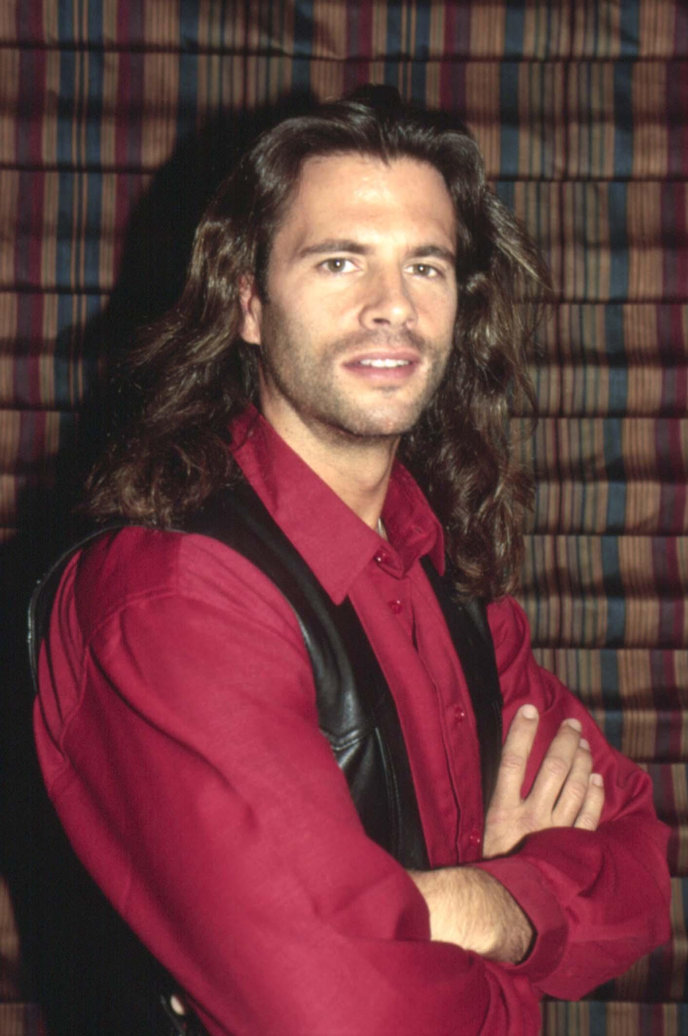 Lorenzo Lamas verkörpert in einem Porträt aus dem Jahr 1993 seine raue „Renegade“-Rolle. Der Schauspieler posiert mit verschränkten Armen vor einem gestreiften Hintergrund und trägt schulterlanges, dunkles, welliges Haar, einen leichten Bartschatten und seinen typischen durchdringenden Blick, während er ein tiefrotes Hemd mit Knöpfen und eine schwarze Lederweste trägt. | Quelle: Getty Images