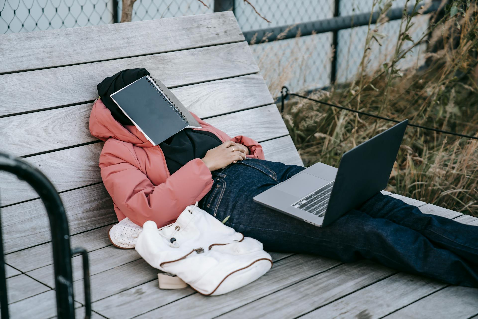 Eine unerkennbare Frau mit einem aufgeklappten Laptop, die sich auf einer Bank ausruht, mit einem Buch im Gesicht | Quelle: Pexels