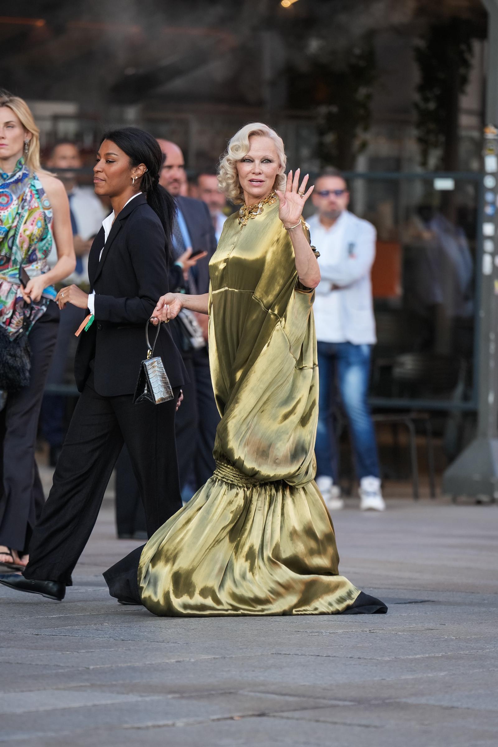 Anderson lächelt und winkt bei ihrer Ankunft in Mailand, während der fließende Stoff ihres metallischen Abendkleids hinter ihr herweht. Ihr Auftritt fand im Rahmen der Mailänder Modewoche für Damenmode Frühjahr/Sommer 2027 statt. | Quelle: Getty Images