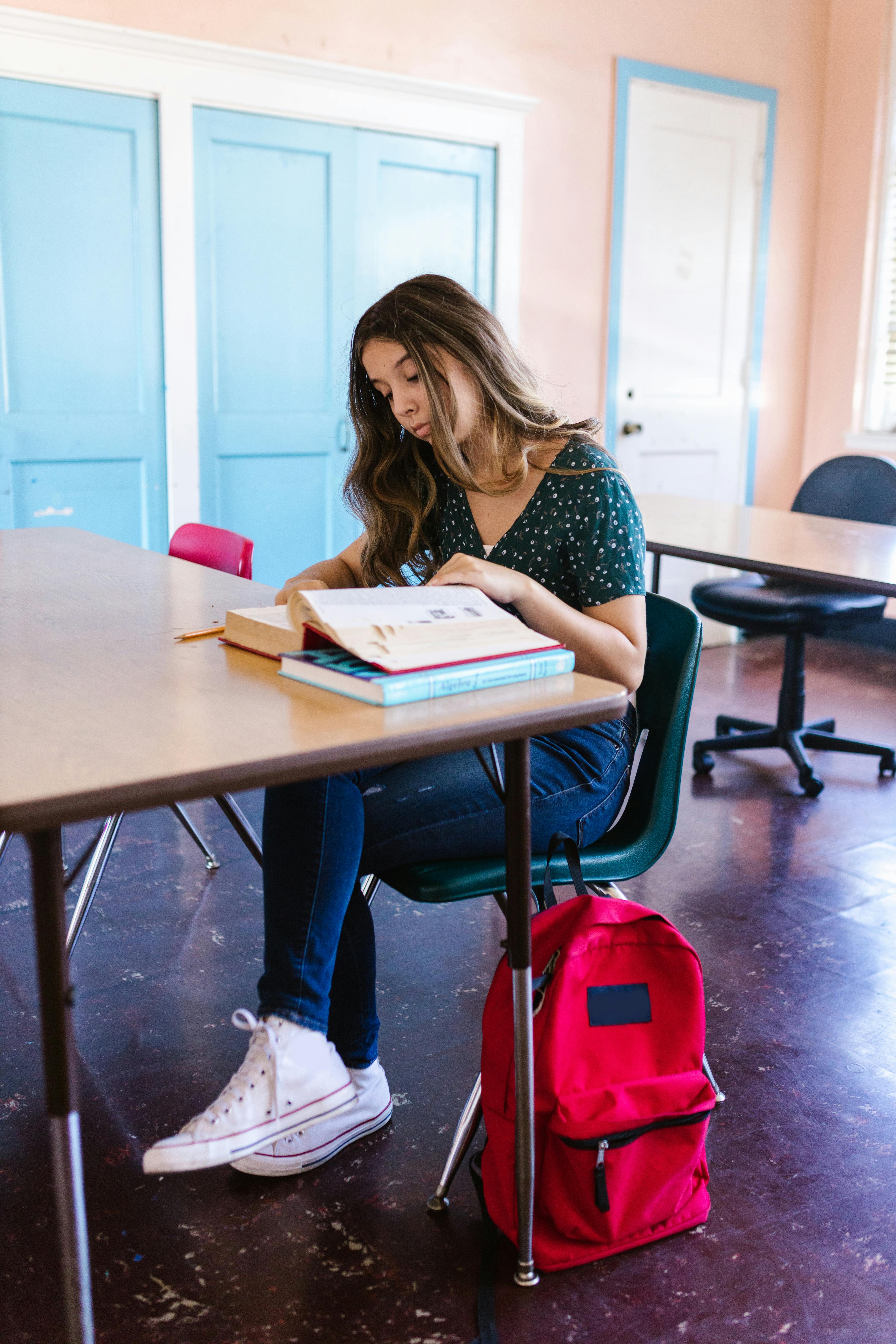 Ein unglückliches Mädchen sitzt an einem Schreibtisch mit einem Buch vor sich in der Schule | Quelle: Pexels