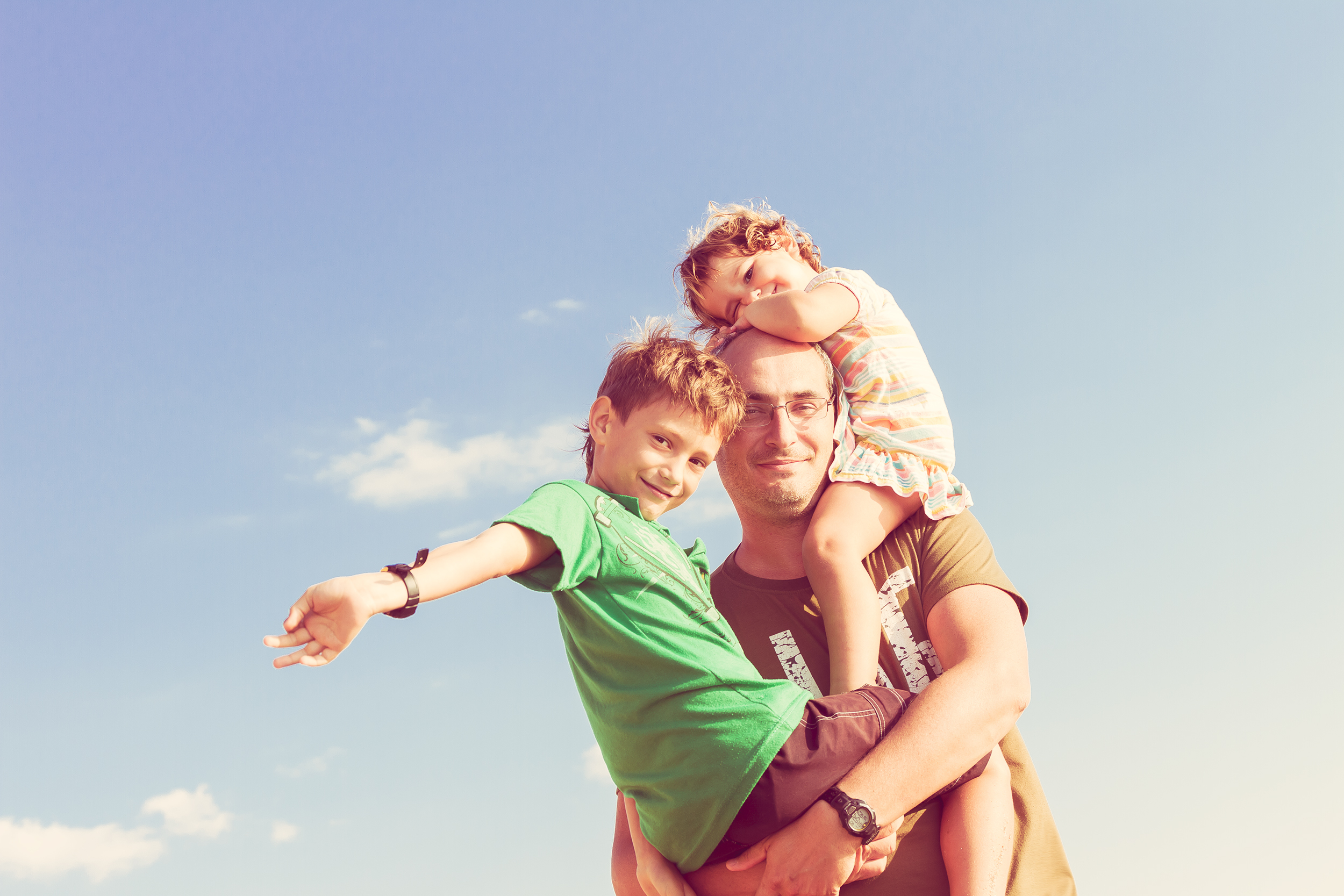 Ein Vater hält seinen Sohn im Arm und seine Tochter auf den Schultern | Quelle: Shutterstock