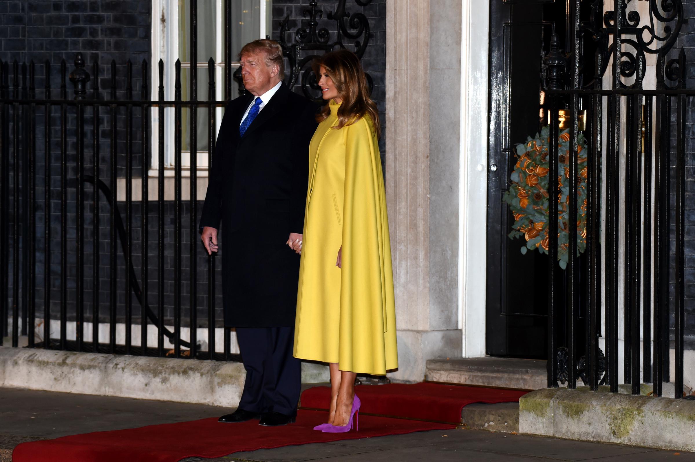 First Lady Melania Trump nimmt im Dezember 2019 am Empfang zum NATO-Gipfel in der Downing Street 10 in London teil und präsentiert dabei einen auffälligen Color-Blocking-Look: einen leuchtend gelben Cape-Mantel von Valentino, kombiniert mit magentafarbenen Wildleder-Stilettos mit spitzer Zehenpartie von Christian Louboutin.