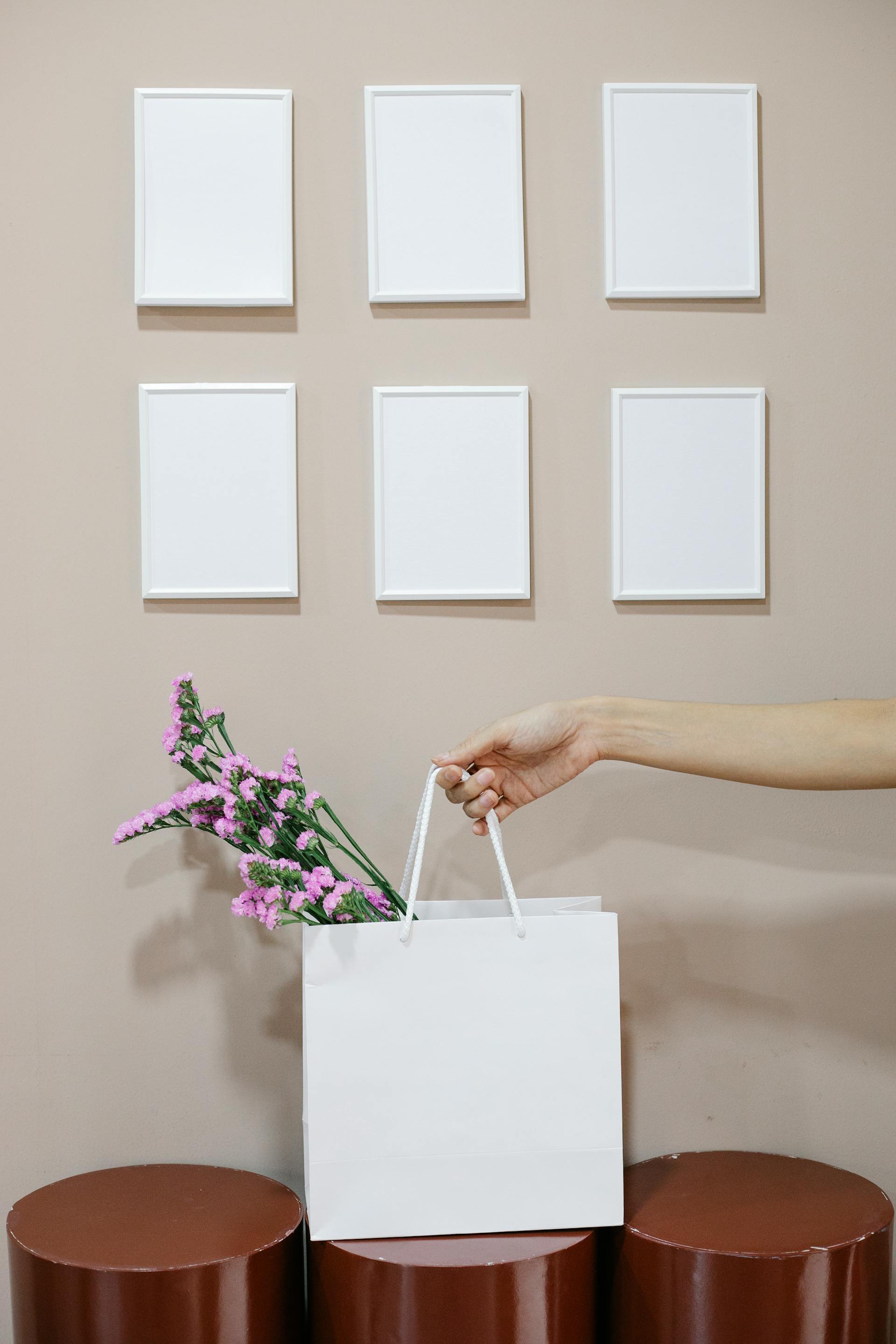 Eine Nahaufnahme einer Frau, die eine Papiertüte mit Blumen in der Nähe einer Wand mit leeren Rahmen hält | Quelle: Pexels
