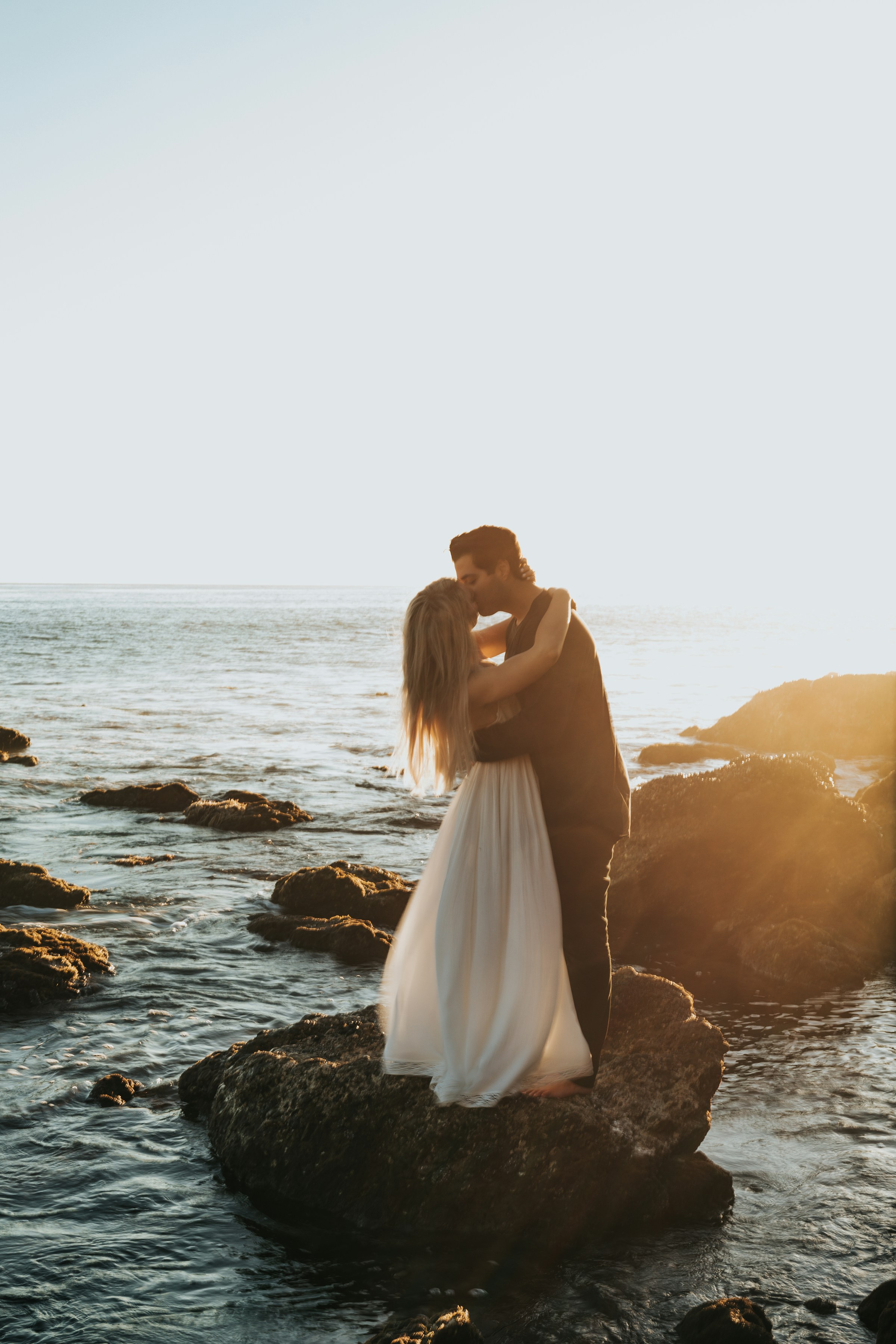 Ein Paar, das sich küsst, während es auf einem Felsen am Strand steht | Quelle: Unsplash