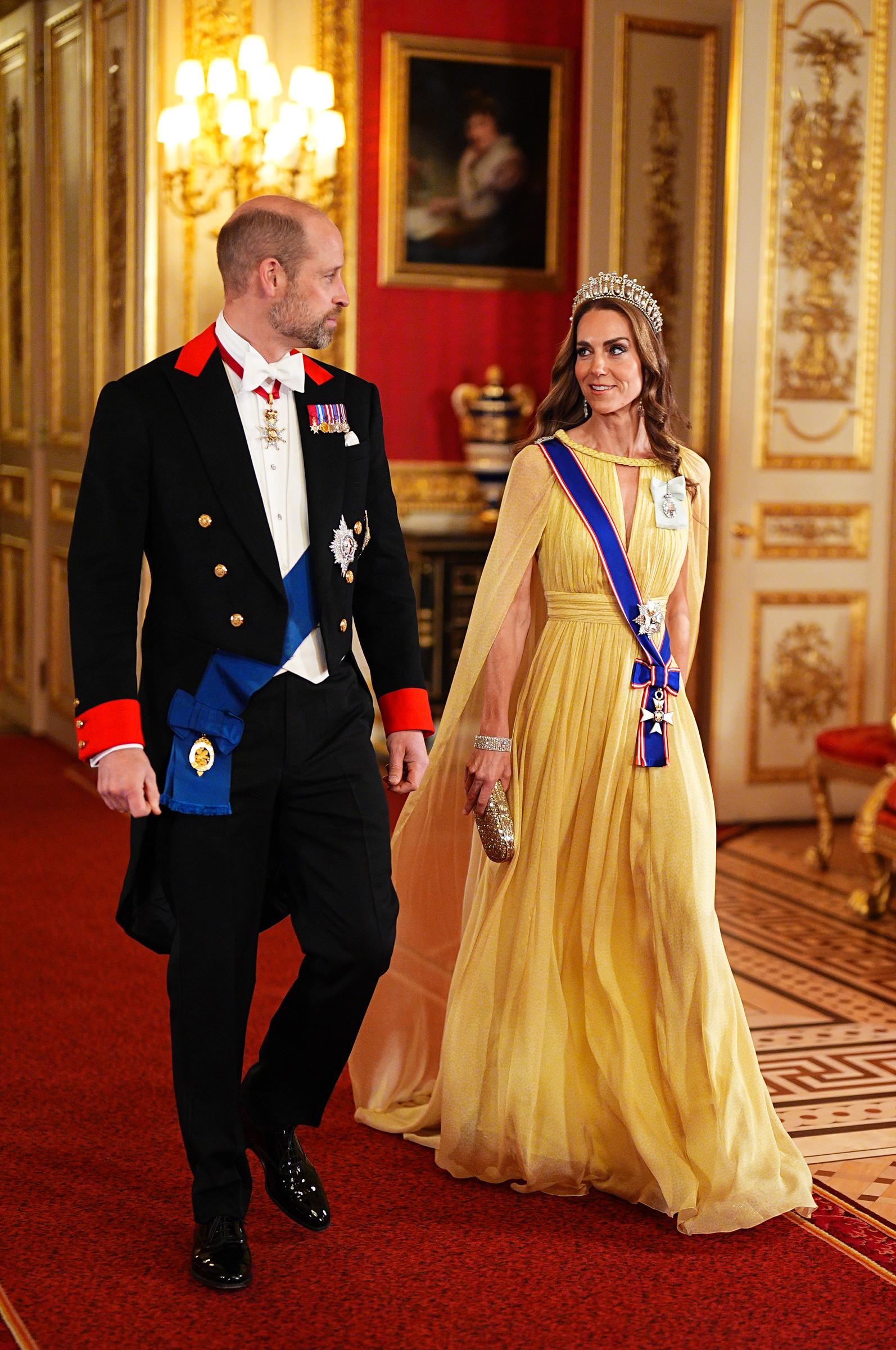 Als der Prinz und die Prinzessin von Wales am 20. Oktober 2026 Seite an Seite durch die mit rotem Teppich ausgelegten Korridore von Windsor Castle schreiten, strahlen sie vor dem festlichen Abendessen königliche Eleganz aus. Catherine schreitet in einem plissierten, pastellgelben Cape-Kleid von Elie Saab dahin und trägt eine funkelnde goldene Abend-Clutch, während Prinz William einen perfekt sitzenden Frack, eine weiße Weste und eine Fliege sowie seine königlichen Strumpfbandorden trägt. | Quelle: Getty Images