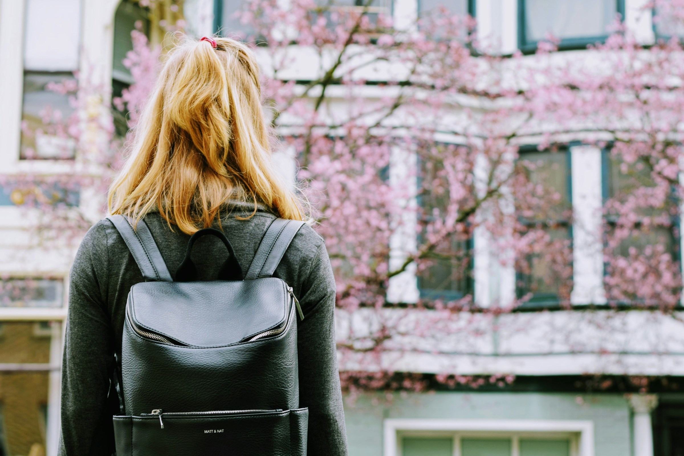 Rückenansicht einer jungen Frau mit Rucksack, die vor einem Gebäude steht | Quelle: Unsplash