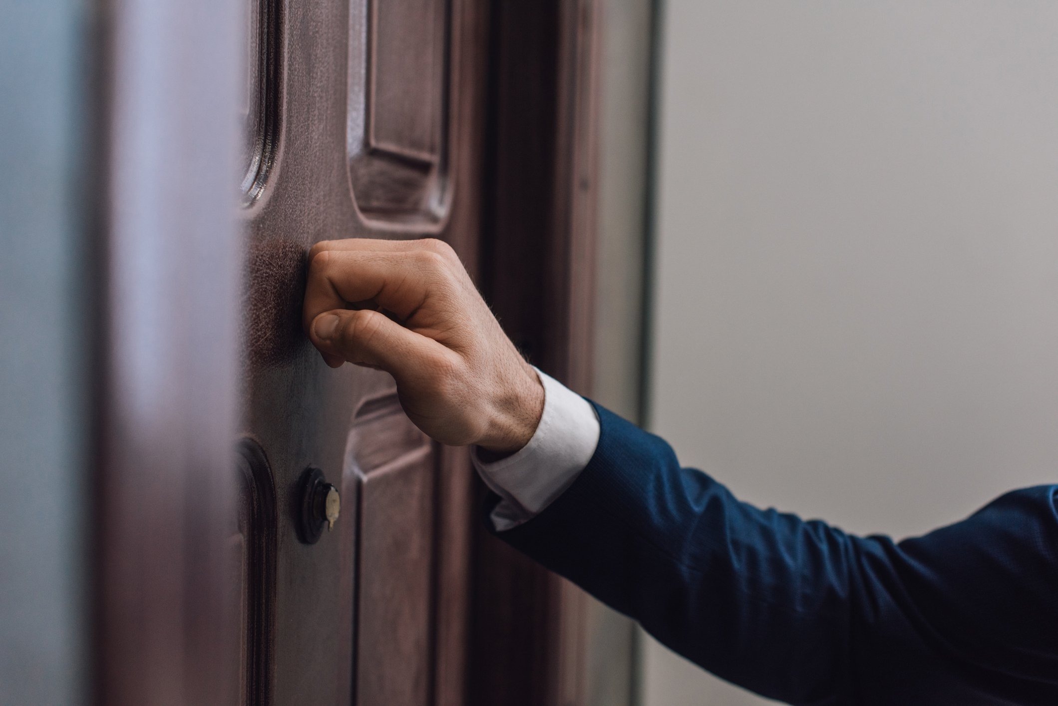 Beschnittene Ansicht des Mannes, der mit der Hand an die Tür klopft  | Quelle: Getty Images