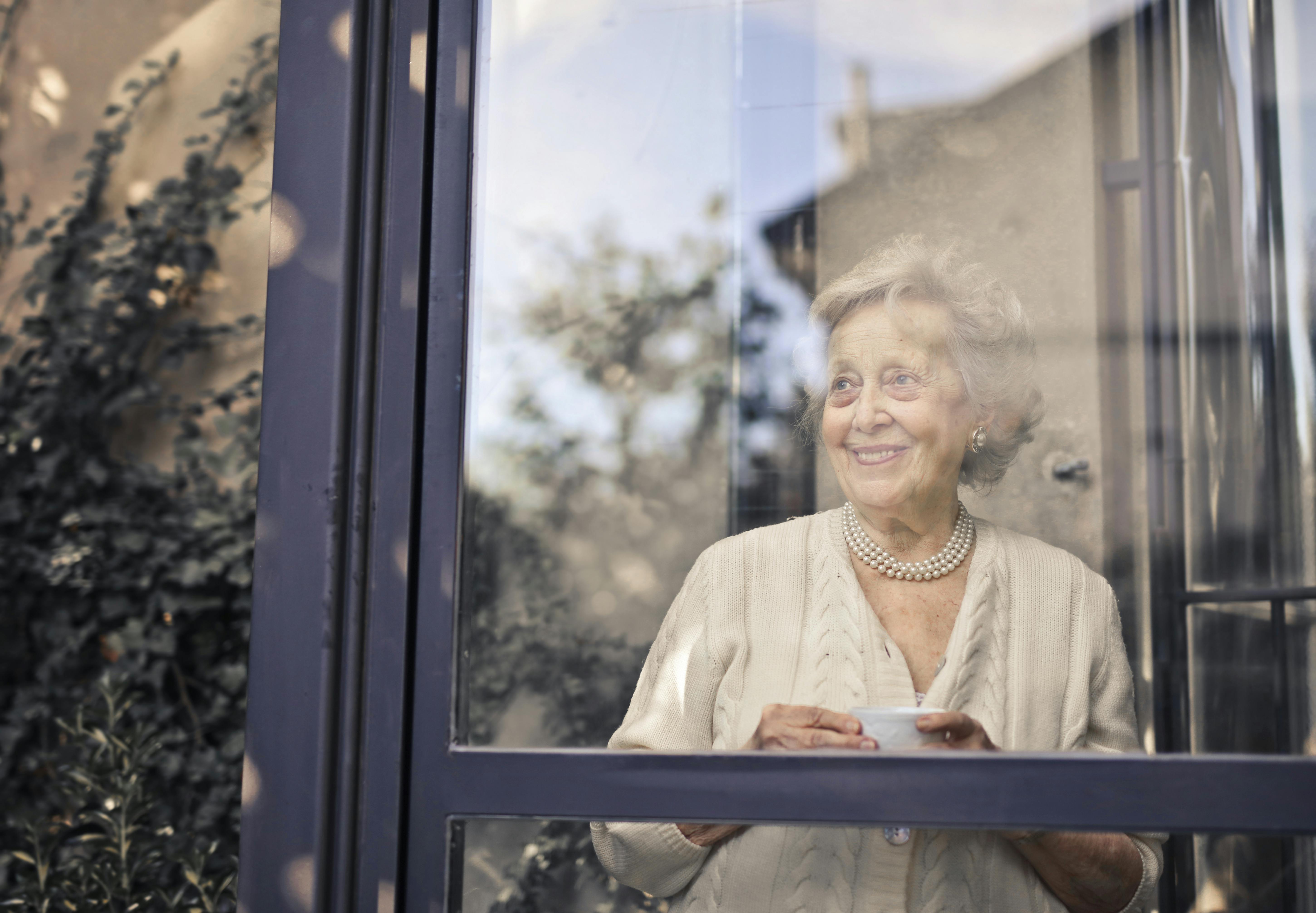 Eine lächelnde ältere Frau, die aus dem Fenster schaut | Quelle: Pexels