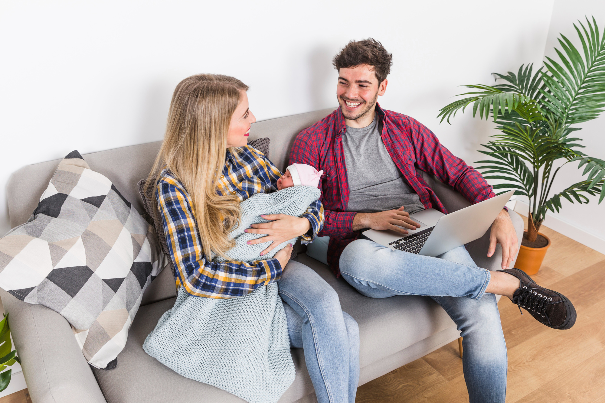 Eine Frau mit einem Baby schaut ihren Mann an, der einen Laptop benutzt | Quelle: Freepik