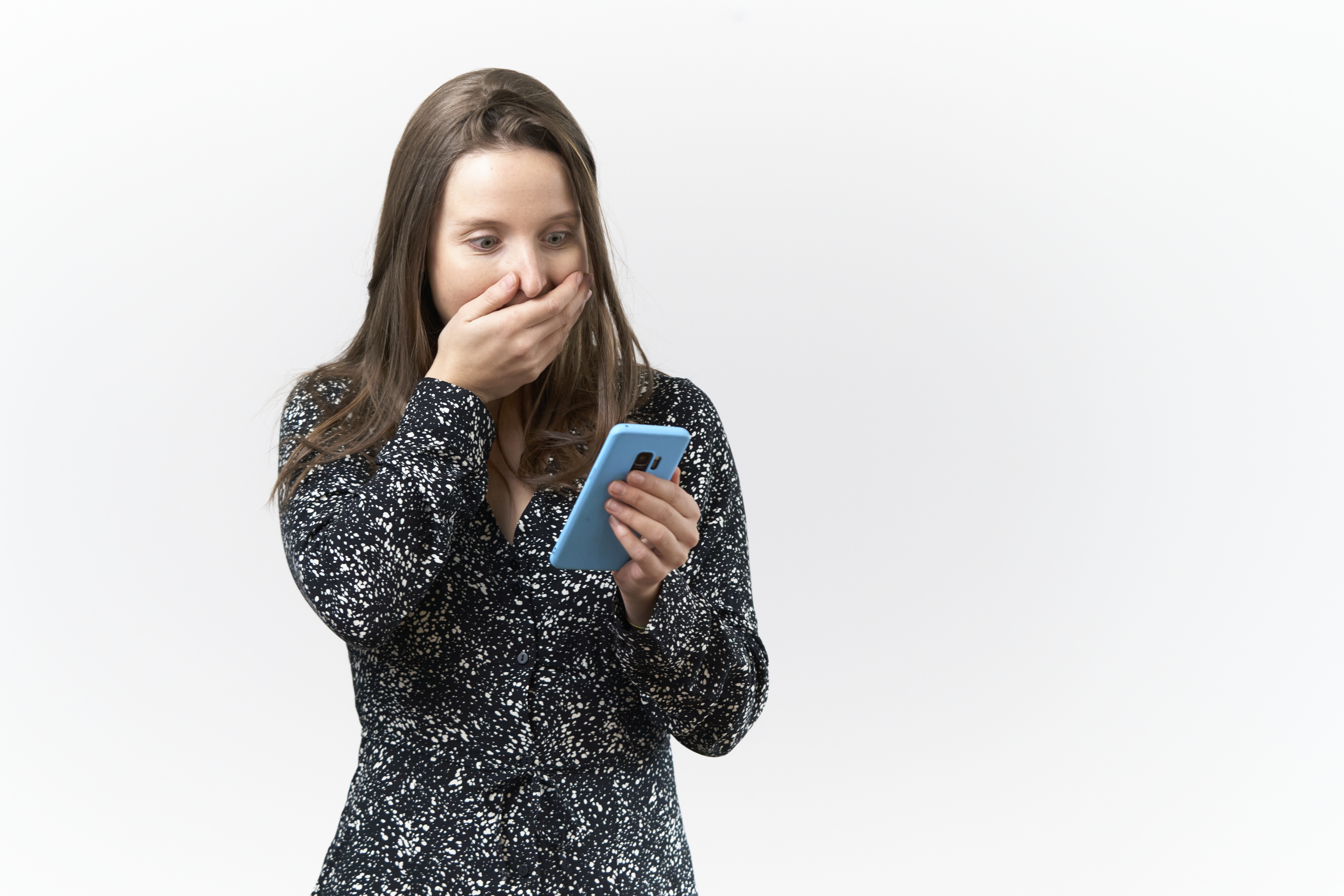 Junge Frau mit überraschtem Gesichtsausdruck liest Nachrichten auf dem Handy vor weißem Hintergrund | Quelle: Getty Images