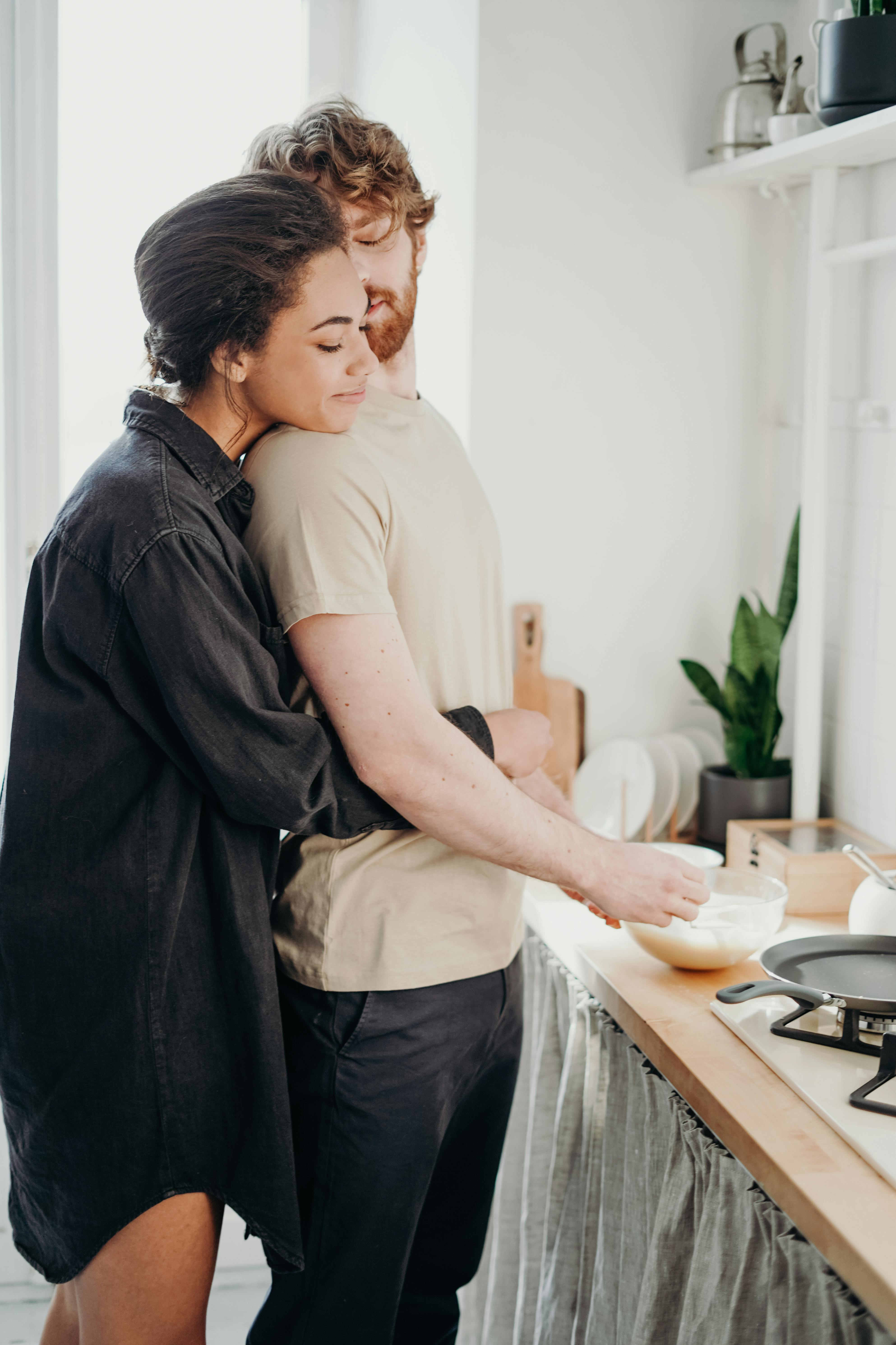 Ein Paar, das sich umarmt, während der Mann eine Mahlzeit zubereitet | Quelle: Pexels