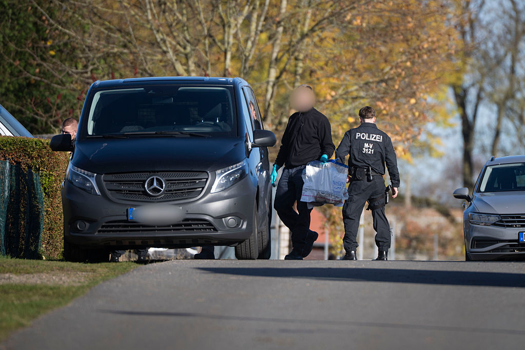 6. November 2025, Mecklenburg-Vorpommern, Güstrow: Ein Ermittler geht während einer Hausdurchsuchung in Reimershagen mit Plastiktüten voller Sportschuhe über die Straße. | Quelle: Getty Images