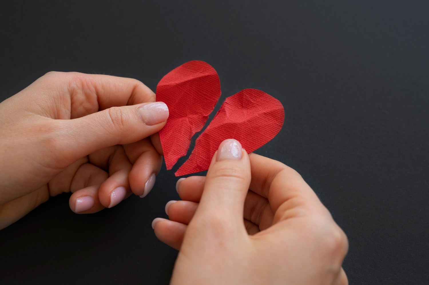 Eine Frau, die ein gebrochenes Papierherz hält | Quelle: Freepik