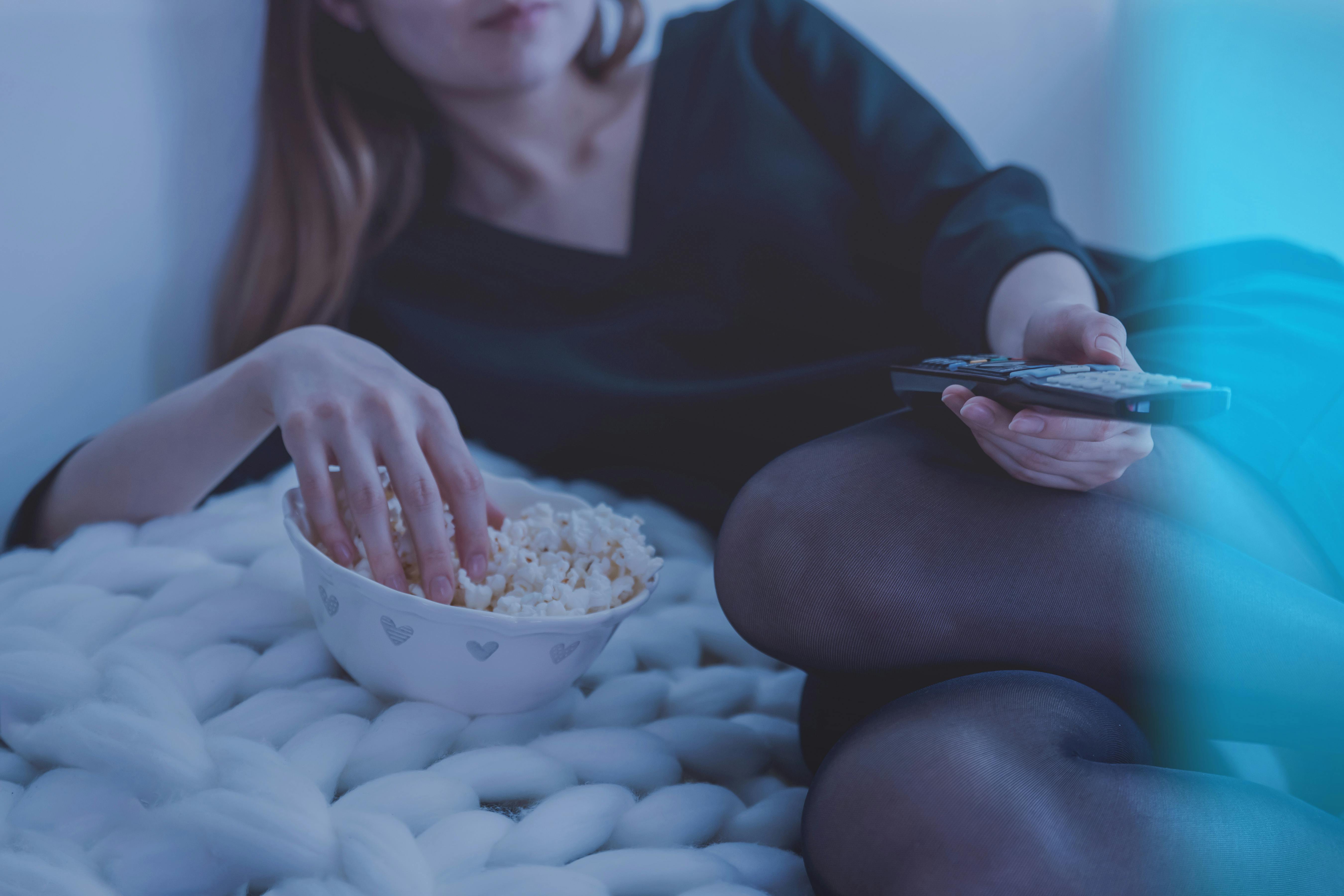 Eine Frau hält eine Fernbedienung, während sie Popcorn isst | Quelle: Pexels