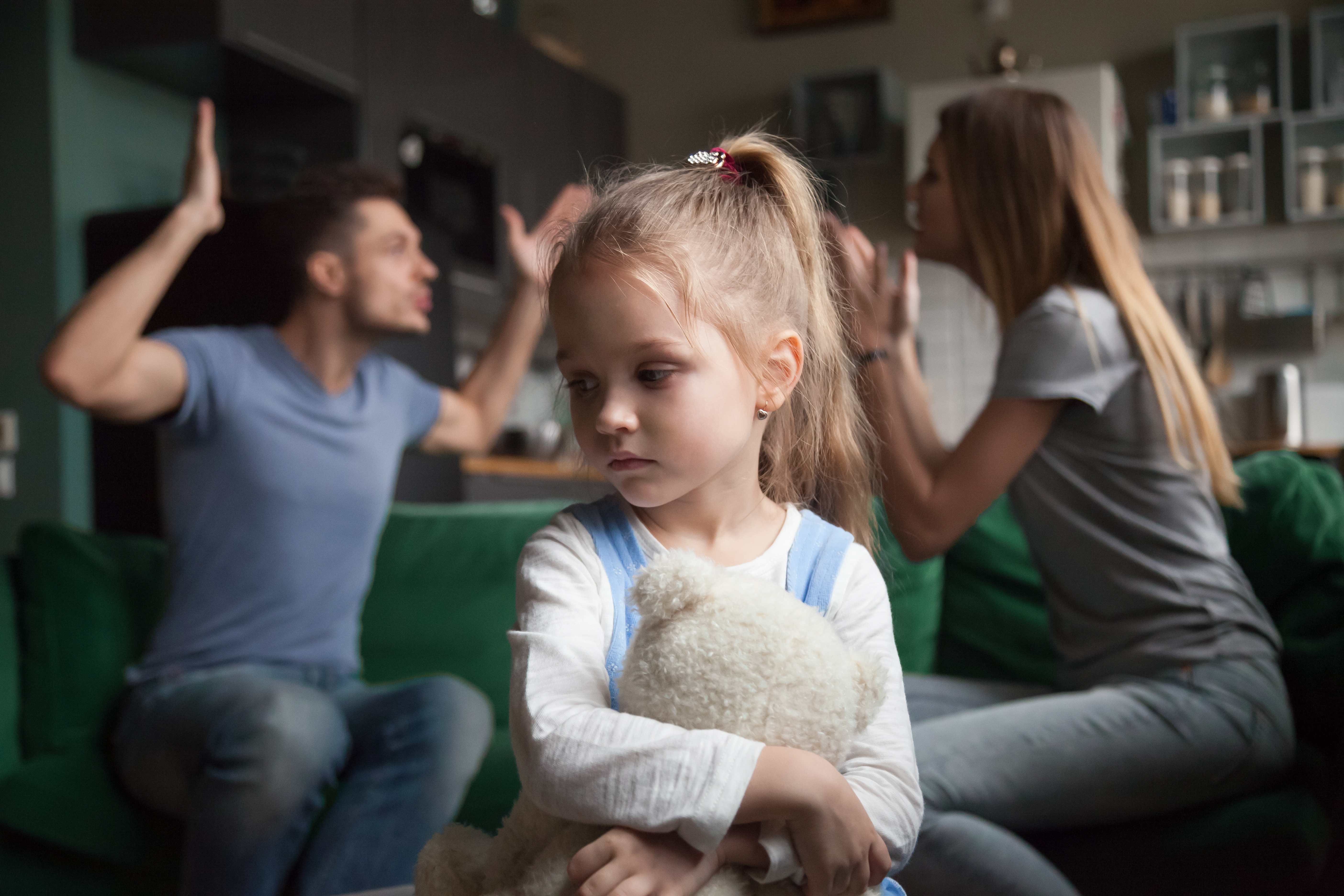 Ein kleines Mädchen, das sich aufregt, während sich seine Eltern im Hintergrund streiten | Quelle: Shutterstock