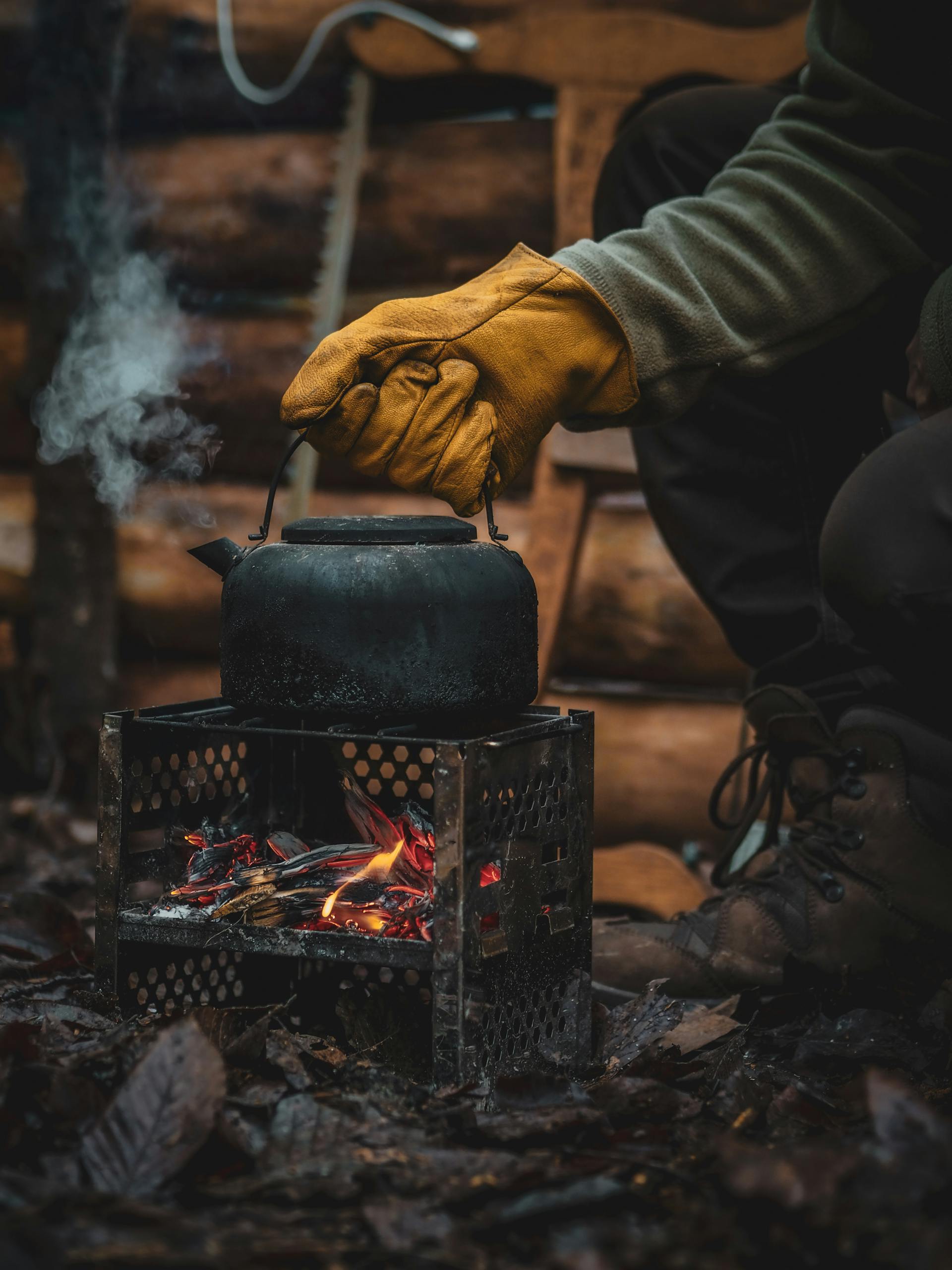 Eine Nahaufnahme einer Person, die einen Handschuh trägt und einen Kessel über das Feuer hält | Quelle: Pexels