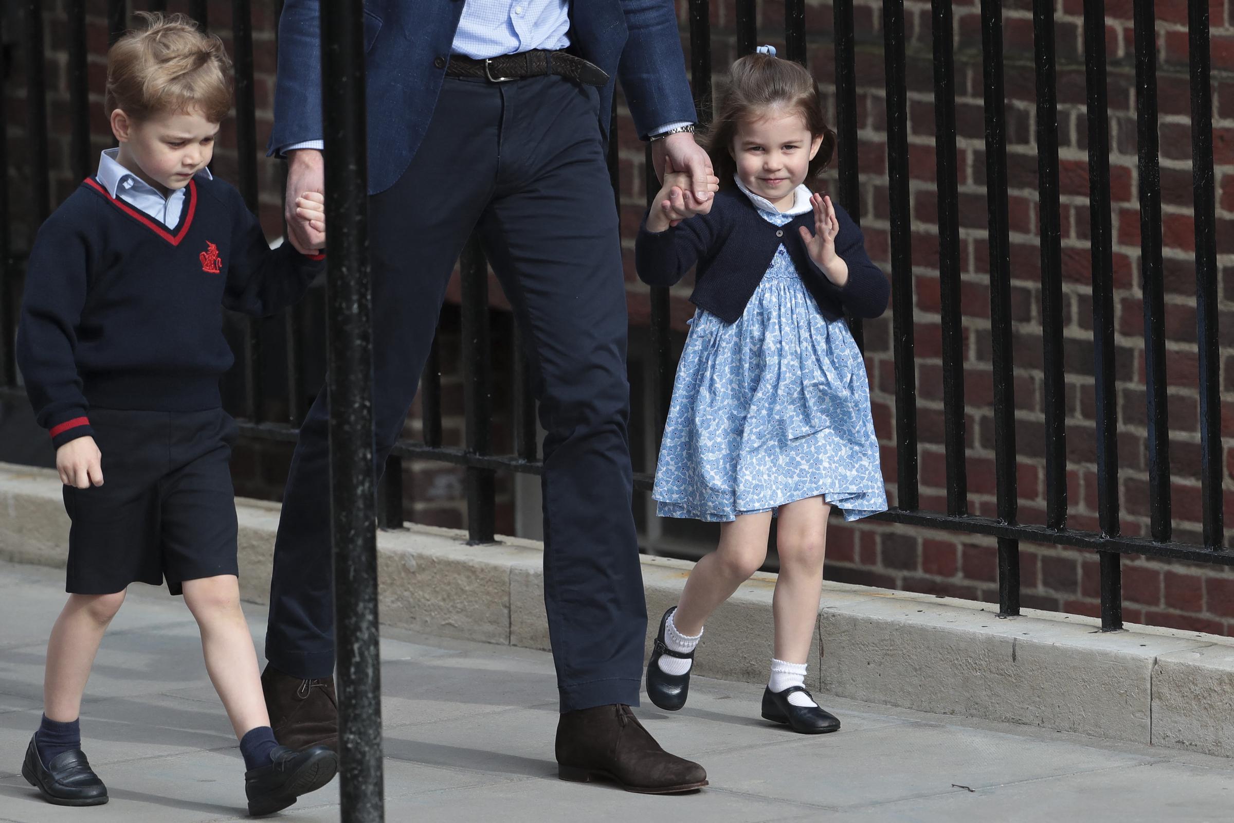 Prinzessin Charlotte von Cambridge winkt den Schaulustigen vor dem Lindo Wing des St. Mary’s Hospital am 23. April 2018 in London, England, liebevoll zu, als sie zusammen mit ihrem Vater Prinz William und ihrem Bruder Prinz George ankommt, um ihren neugeborenen kleinen Bruder zu begrüßen. Die kleine Prinzessin sieht bezaubernd aus in einem blau-weißen Smockkleid mit Blumenmuster, dazu eine marineblaue Strickjacke, weiße Socken und Mary-Jane-Schuhe, während sie die Hand ihres Vaters hält. | Quelle: Getty Images