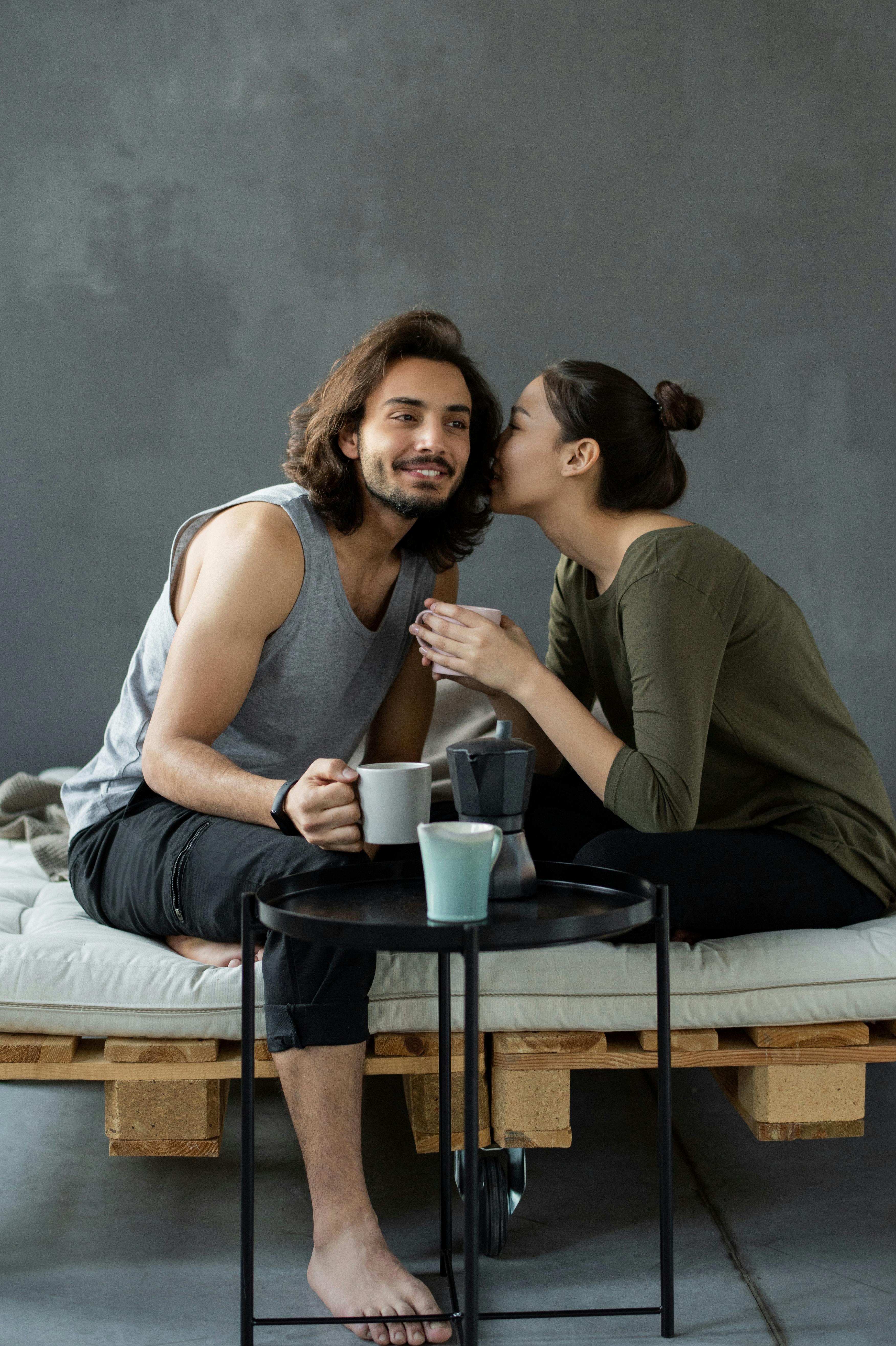 Ein Mann lächelt, während eine Frau ihm bei einem Getränk etwas zuflüstert | Quelle: Pexels