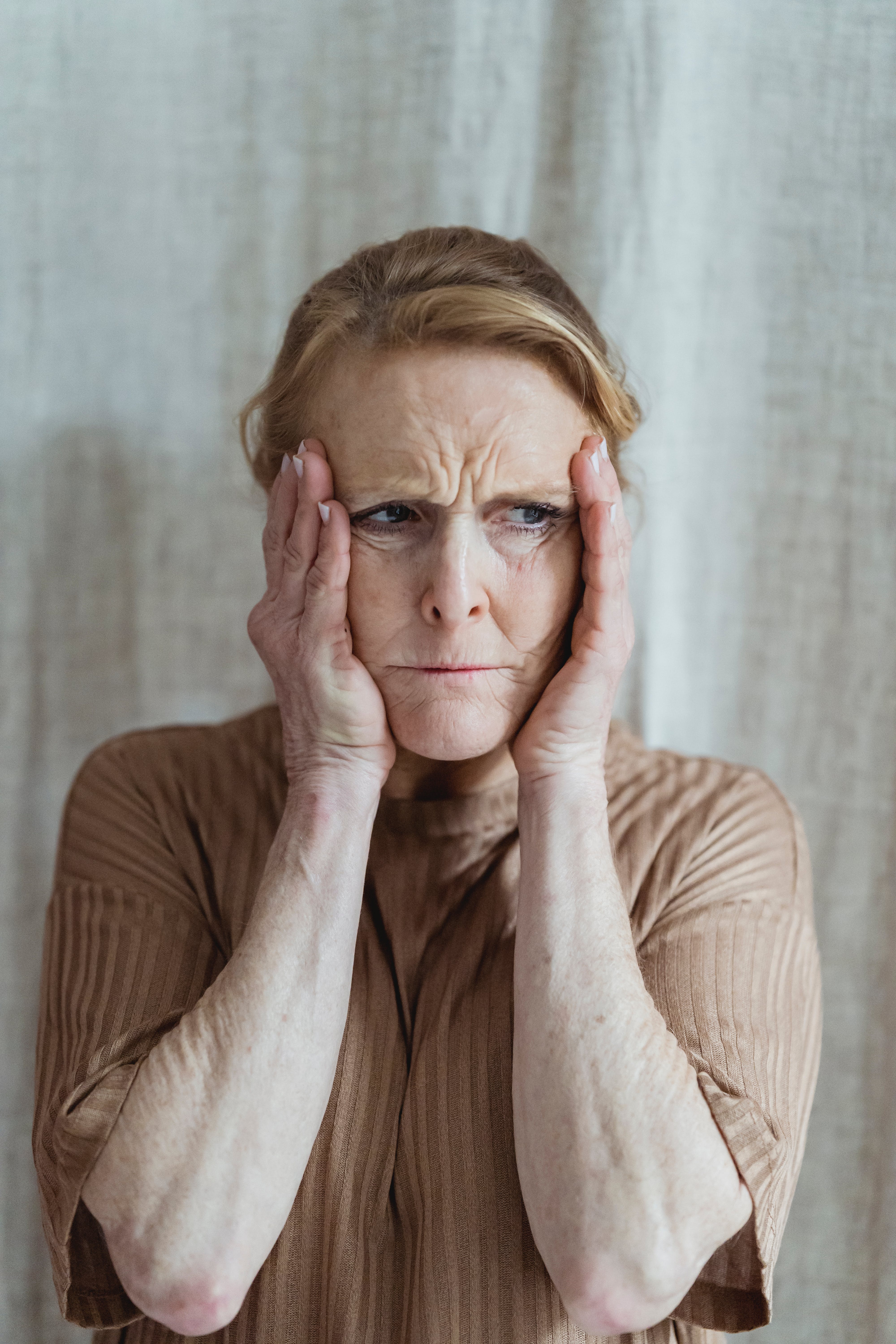 Eine verzweifelte ältere Frau, die sich mit beiden Händen das Gesicht hält | Quelle: Pexels