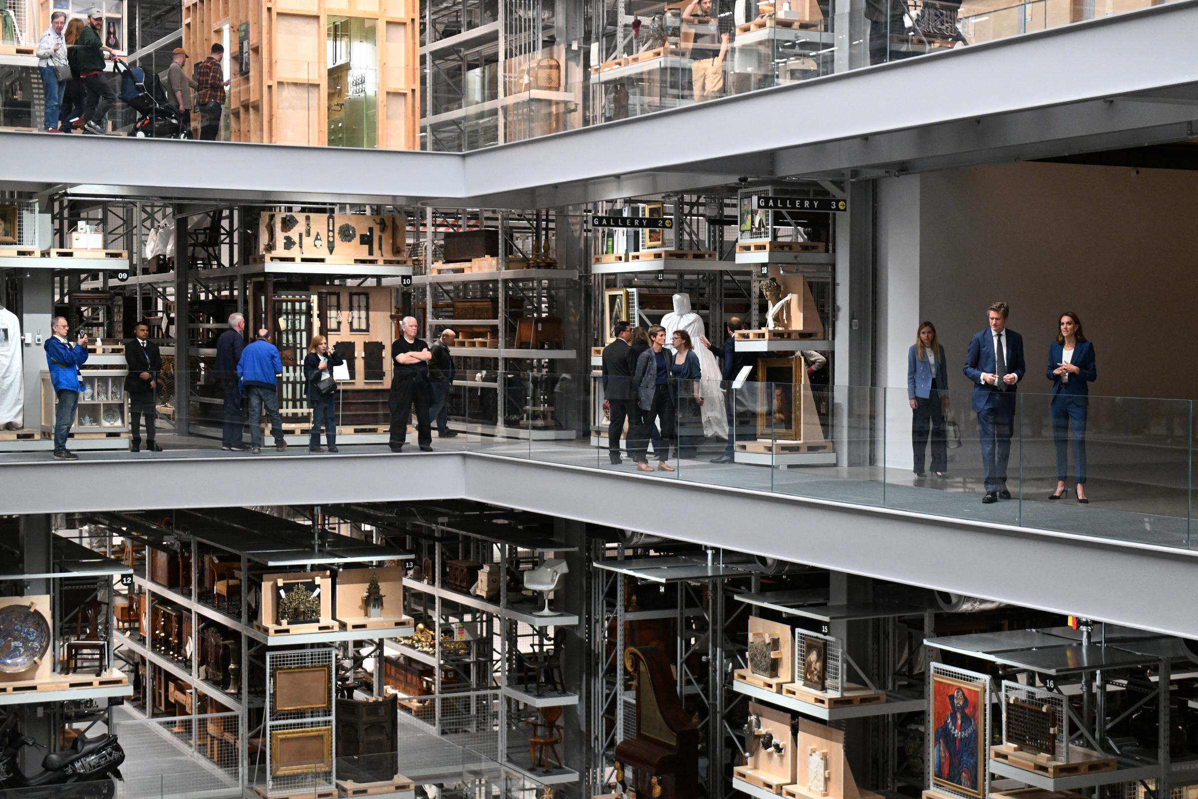 Aus der Ferne betrachtet, geht Prinzessin Catherine neben Tristram Hunt durch das Zwischengeschoss der Galerie. Regale mit Kunst und Artefakten säumen den Weg. Sie hört aufmerksam zu, ihr Blick ist ruhig und aufmerksam.