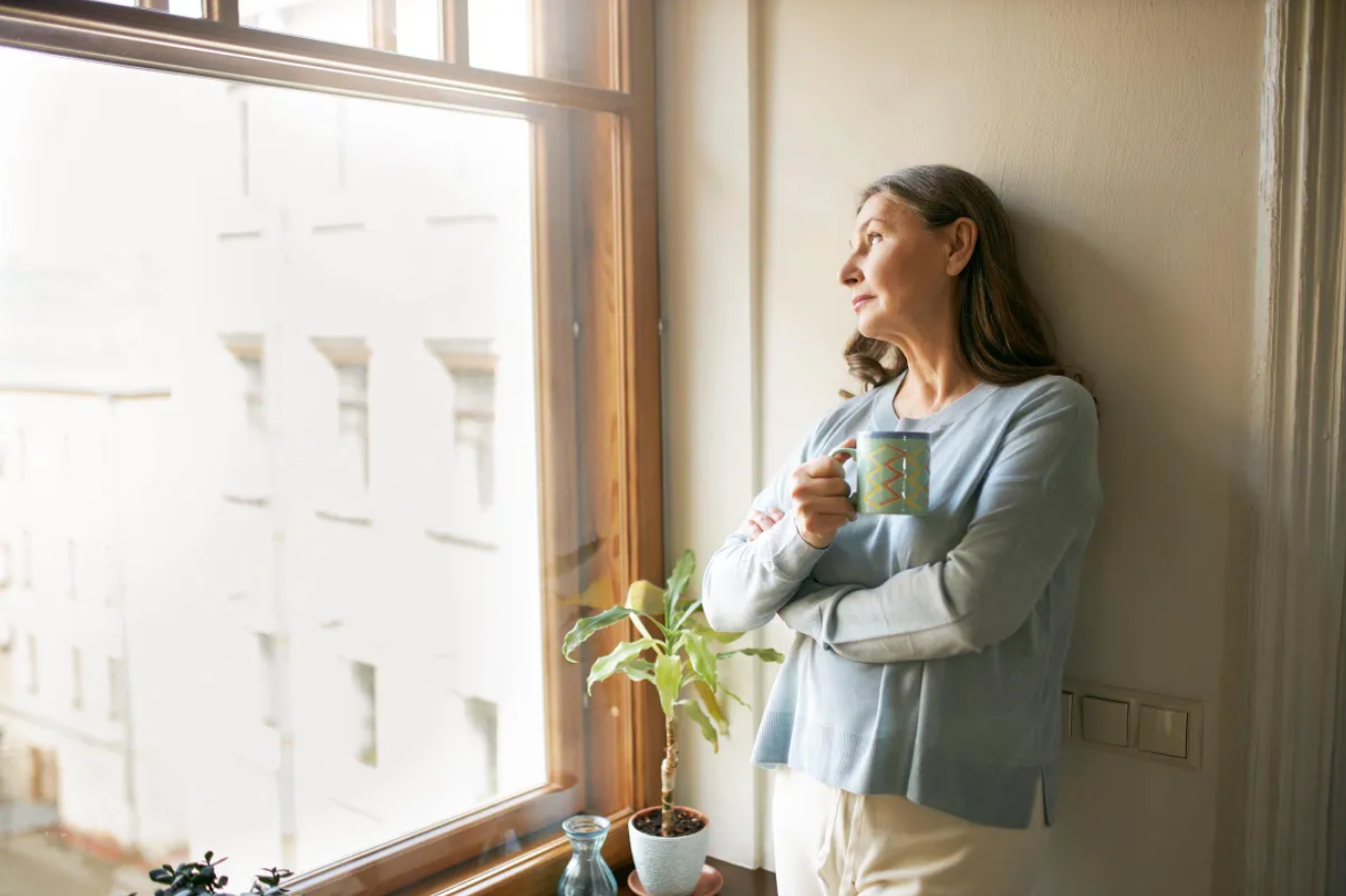 Reife Frau steht am Fenster | Quelle: Freepik